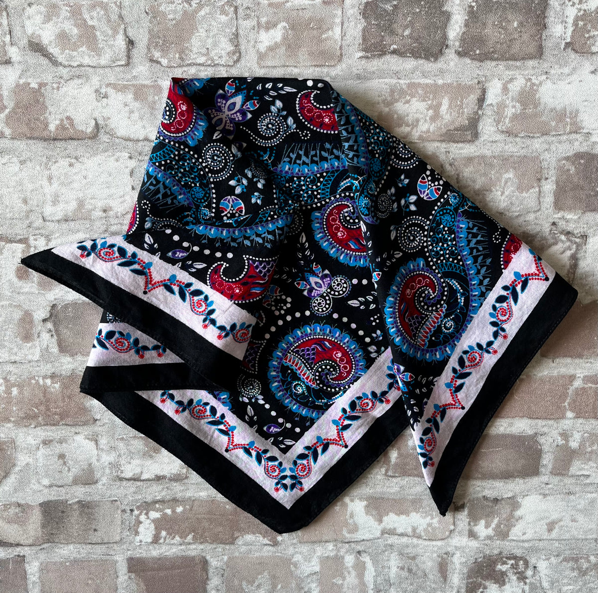 Bandana en coton vintage des années 90 au motif Paisley psychédélique turquoise et rouge sur fond noir, présenté plié à plat.
