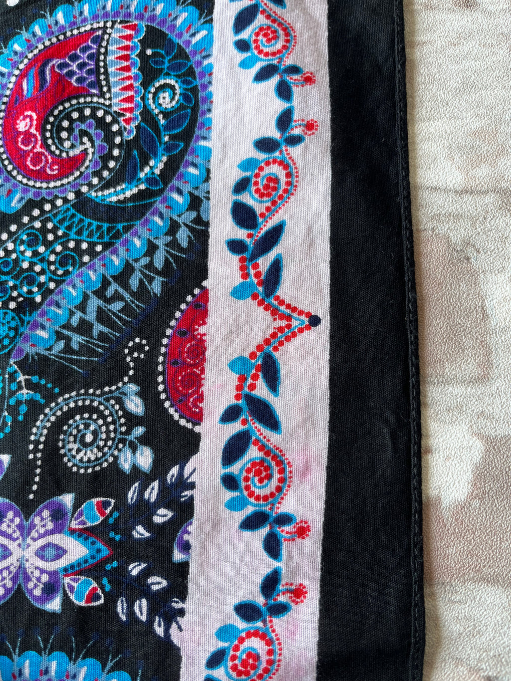 Bandana en coton vintage des années 90 au motif Paisley psychédélique turquoise et rouge sur fond noir, présenté plié à plat. / Gros plan décoloration - transfert couleurs