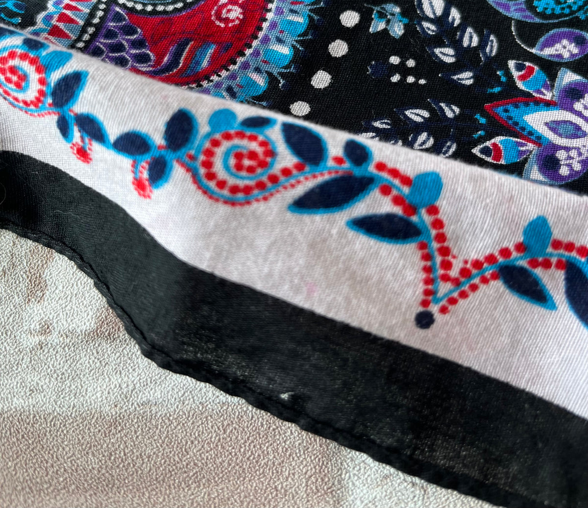 Bandana en coton vintage des années 90 au motif Paisley psychédélique turquoise et rouge sur fond noir, présenté plié à plat / Détail micro accroc