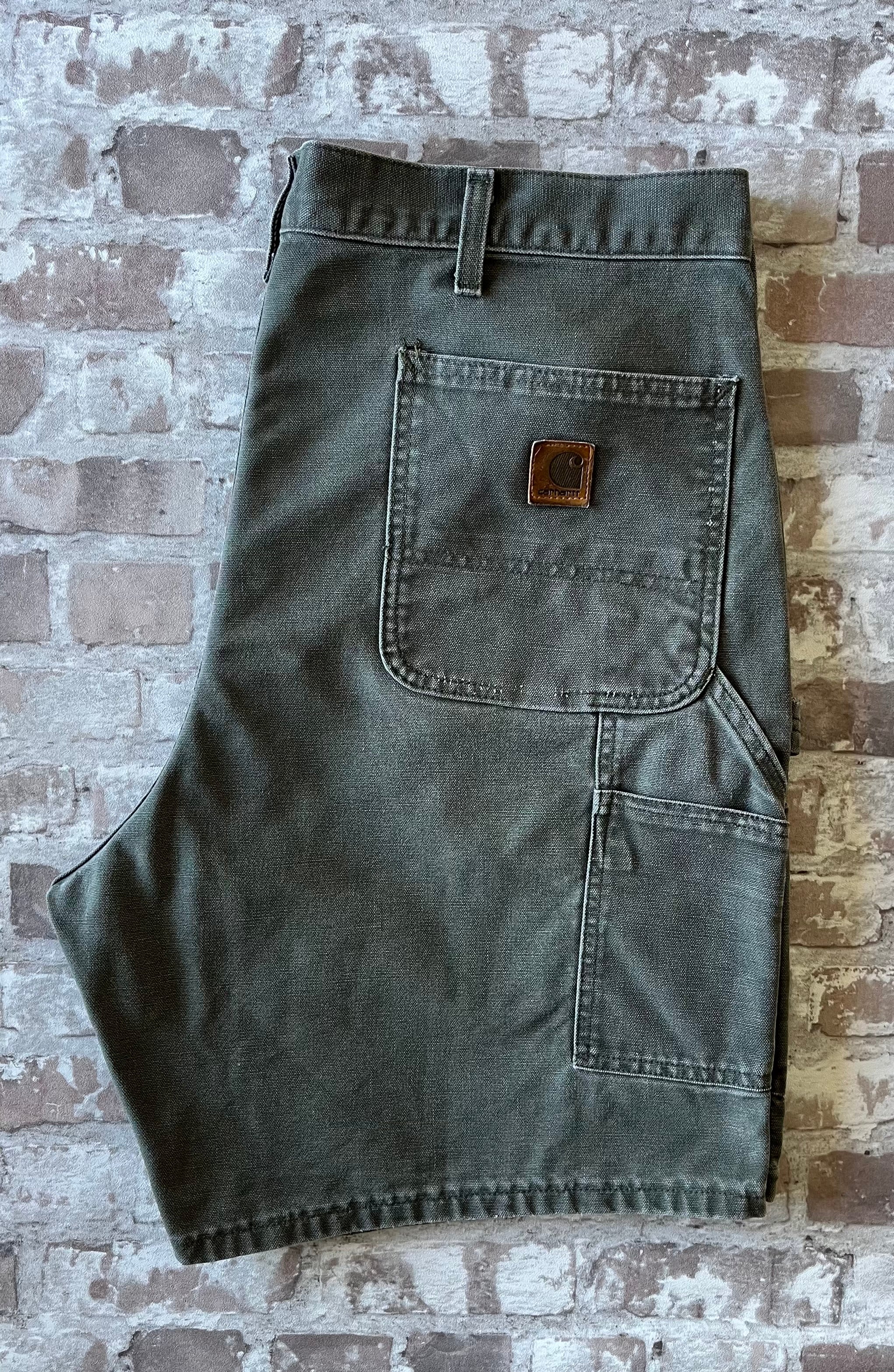 Plan sur la poche arrière droite avant restauration et le patch logo Carhartt en cuir véritable patiné d'un short vintage.
