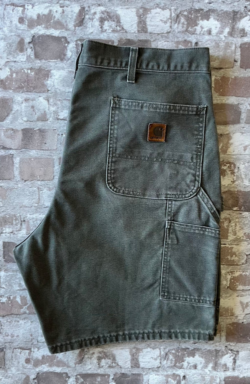 Plan sur la poche arrière droite avant restauration et le patch logo Carhartt en cuir véritable patiné d'un short vintage.