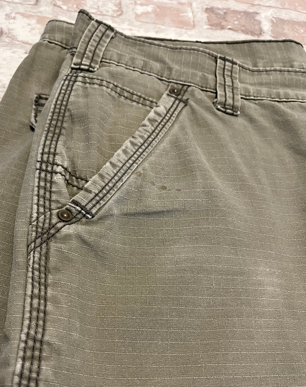Gros plan sur de légers éclats de résine/vernis et la patine d'usage sur la poche d'un short cargo Carhartt de seconde main.