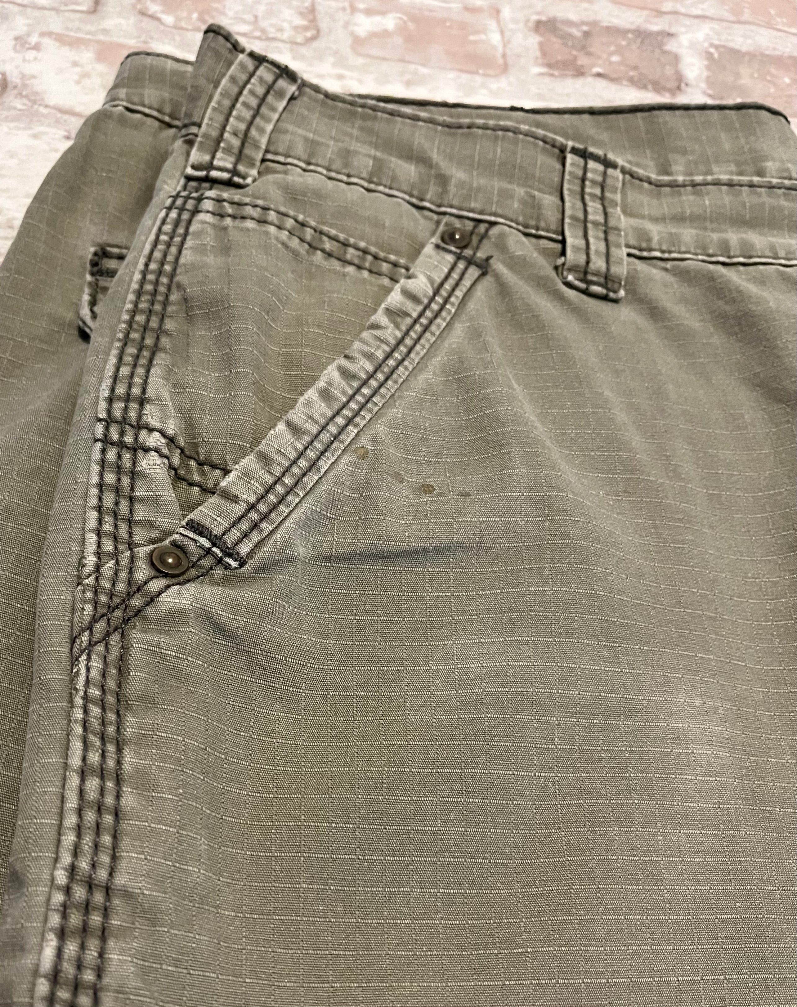 Gros plan sur de légers éclats de résine/vernis et la patine d'usage sur la poche d'un short cargo Carhartt de seconde main.