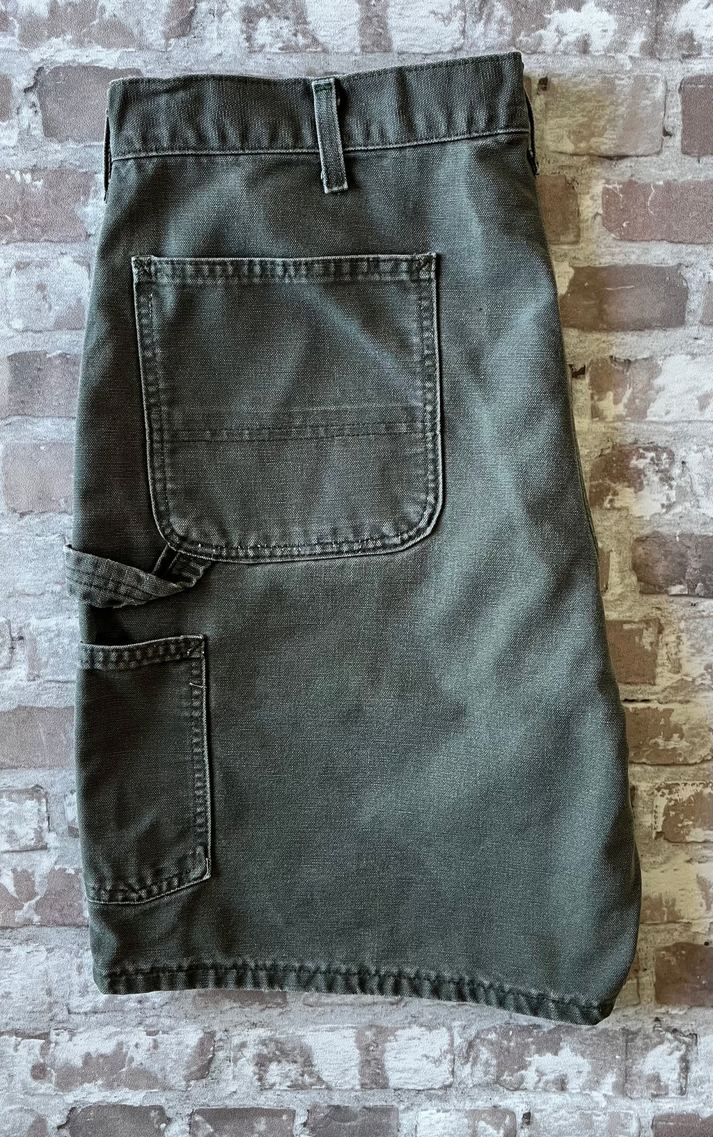 Bermuda de travail vert Moss Carhartt B25 à plat, mettant en valeur la toile en coton canvas délavée et la boucle marteau.