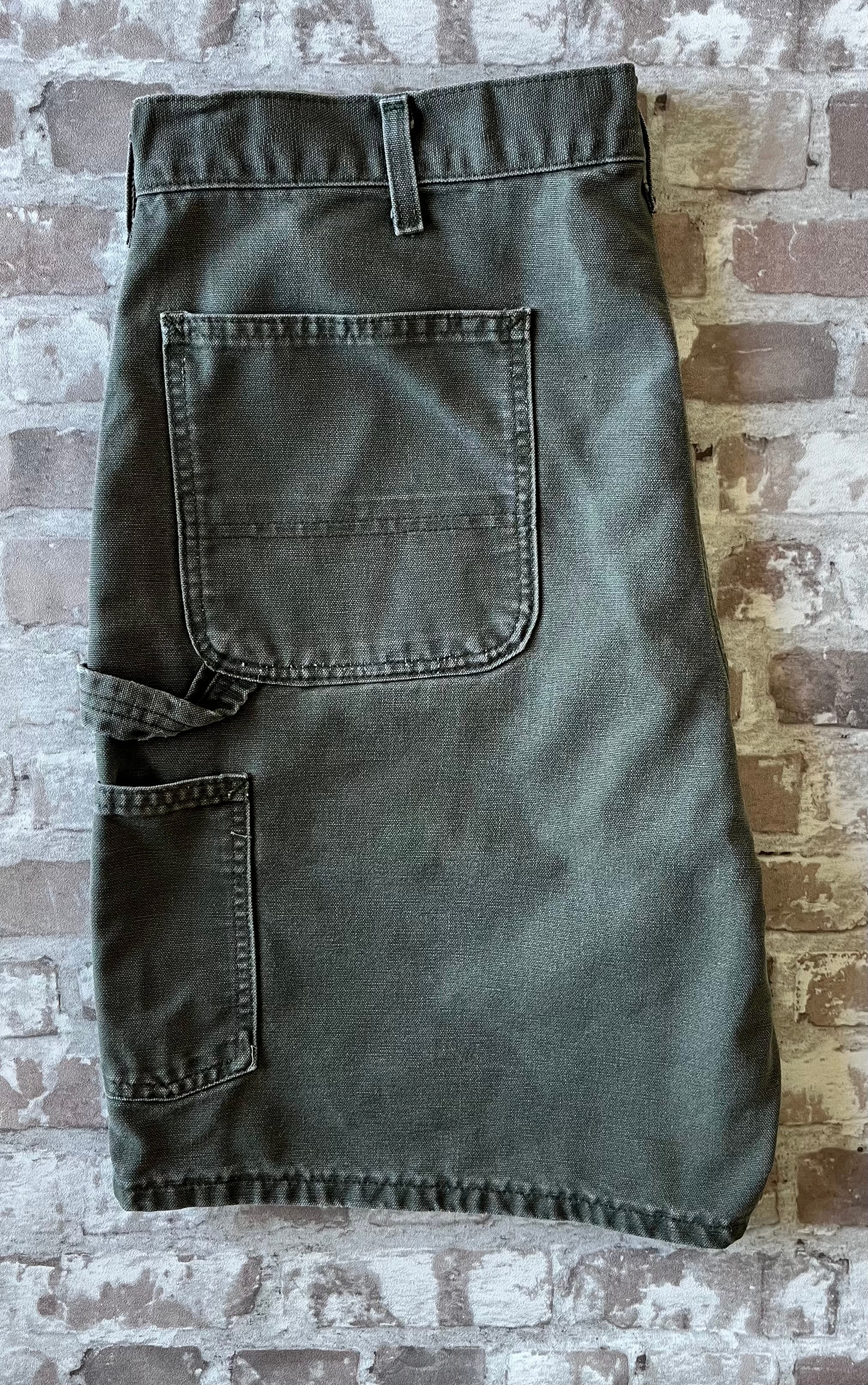 Bermuda de travail vert Moss Carhartt B25 à plat, mettant en valeur la toile en coton canvas délavée et la boucle marteau.