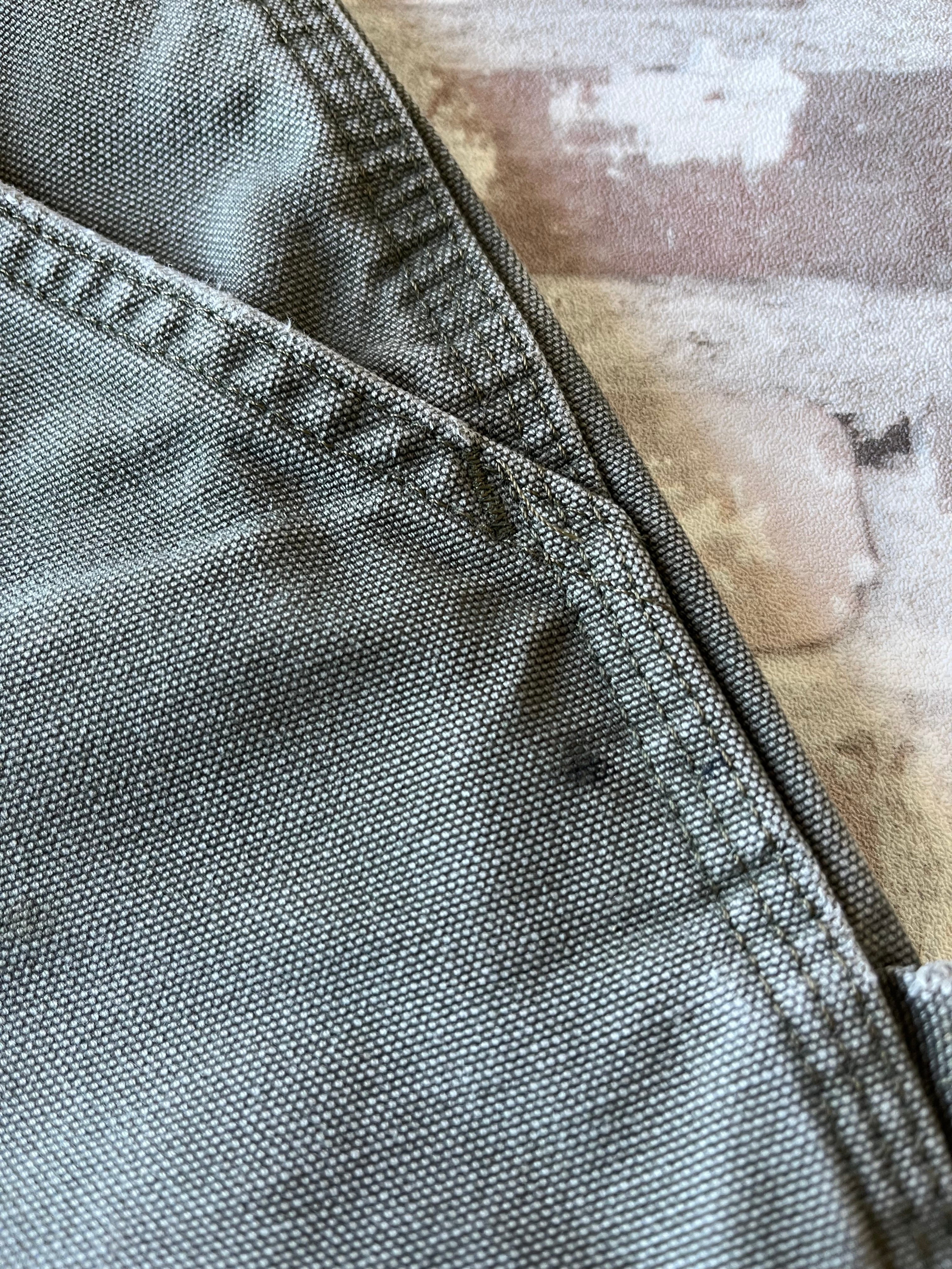 Bermuda de travail vert Moss Carhartt B25 à plat, mettant en valeur la toile en coton canvas délavée et la boucle marteau, focus tache noire proche poche
