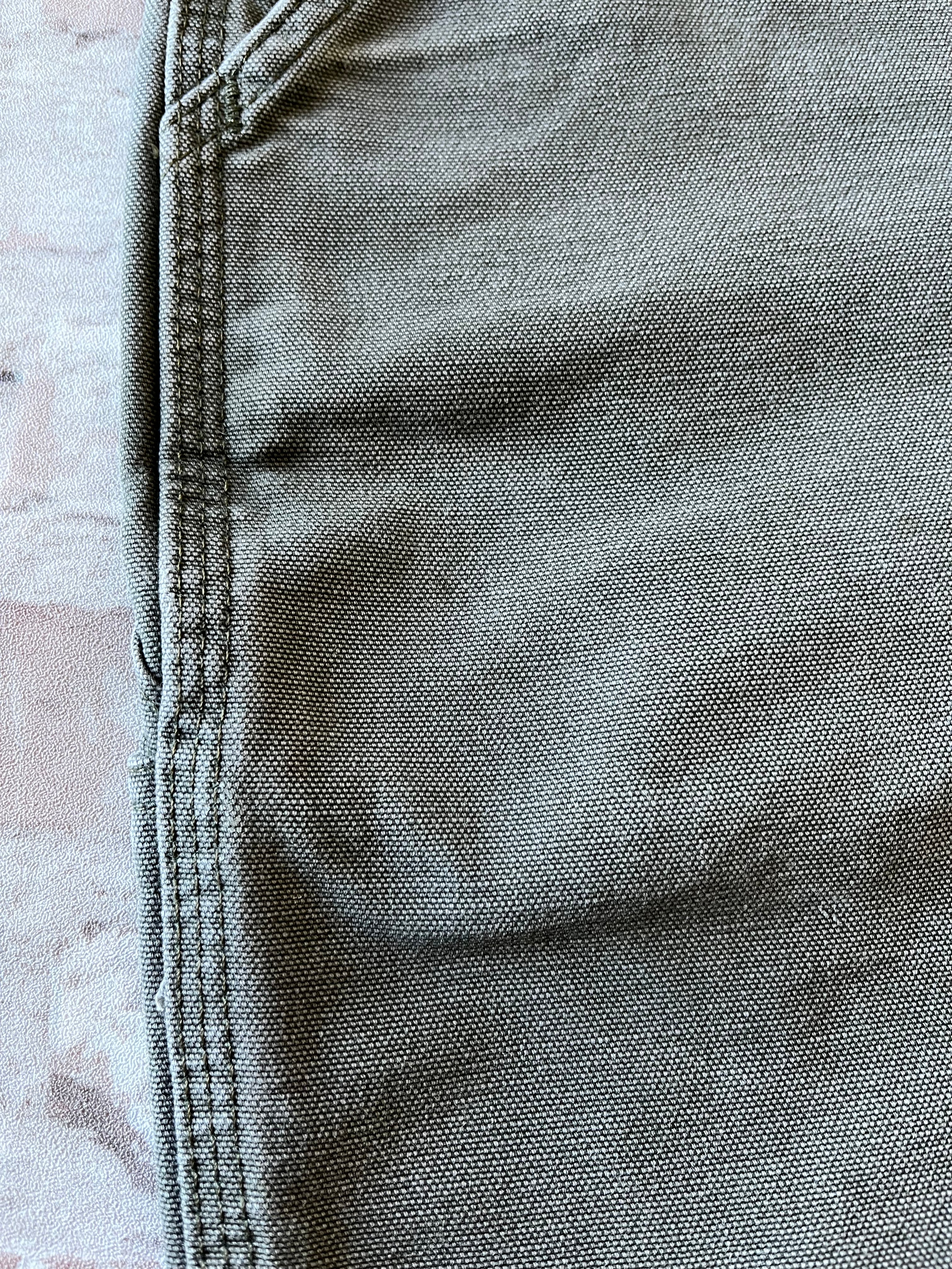 Bermuda de travail vert Moss Carhartt B25 à plat, mettant en valeur la toile en coton canvas délavée et la boucle marteau, focus tache proche poche