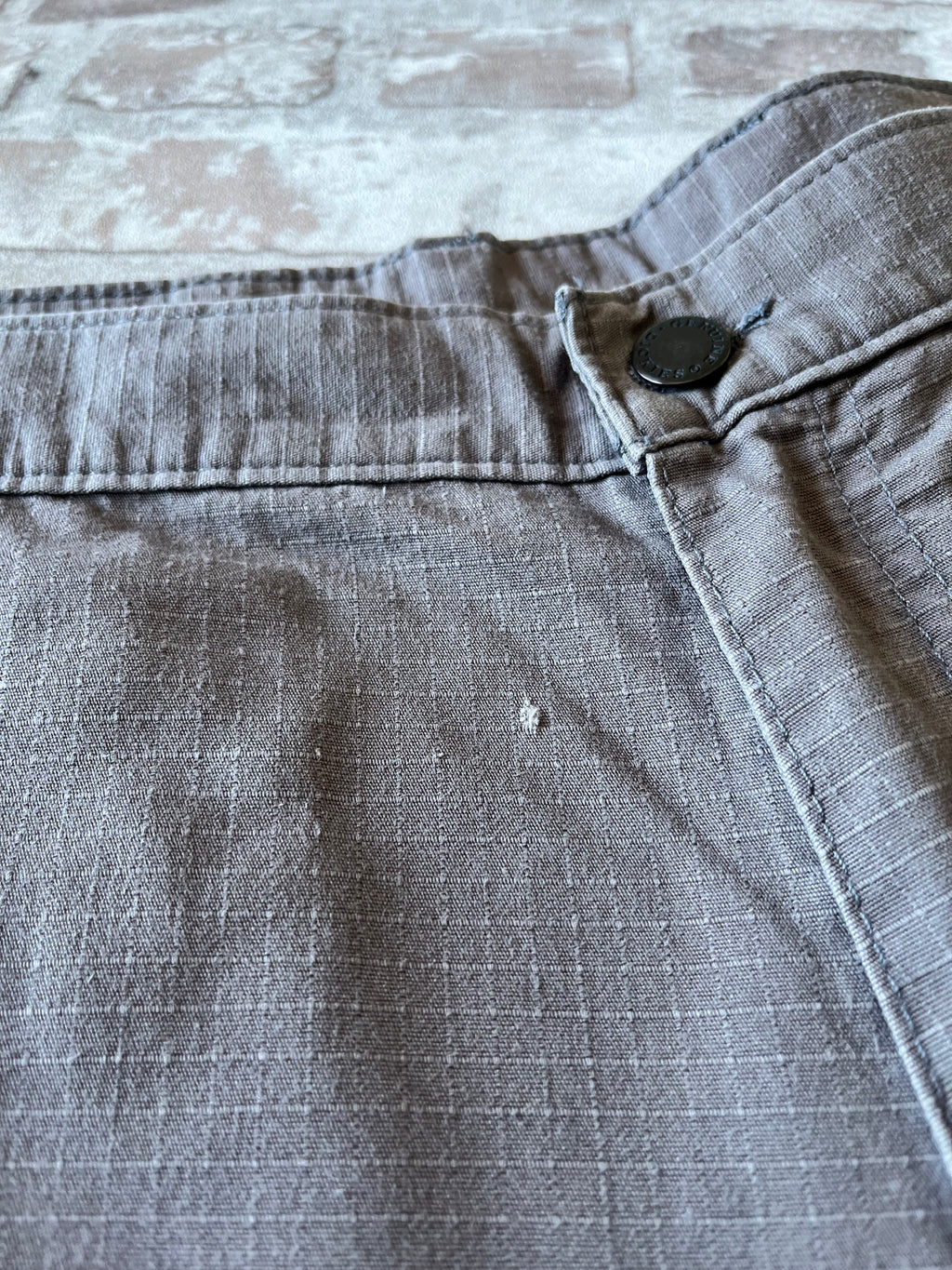 Gros plan sur un petit accroc de la toile patiné d'un short Dickies gris de seconde main