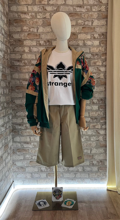 Coupe-vent vintage vert forêt à fleurs On Your Mark porté avec un t-shirt Stranger Things, un bermuda Dickies beige et des patchs La Barbuda.