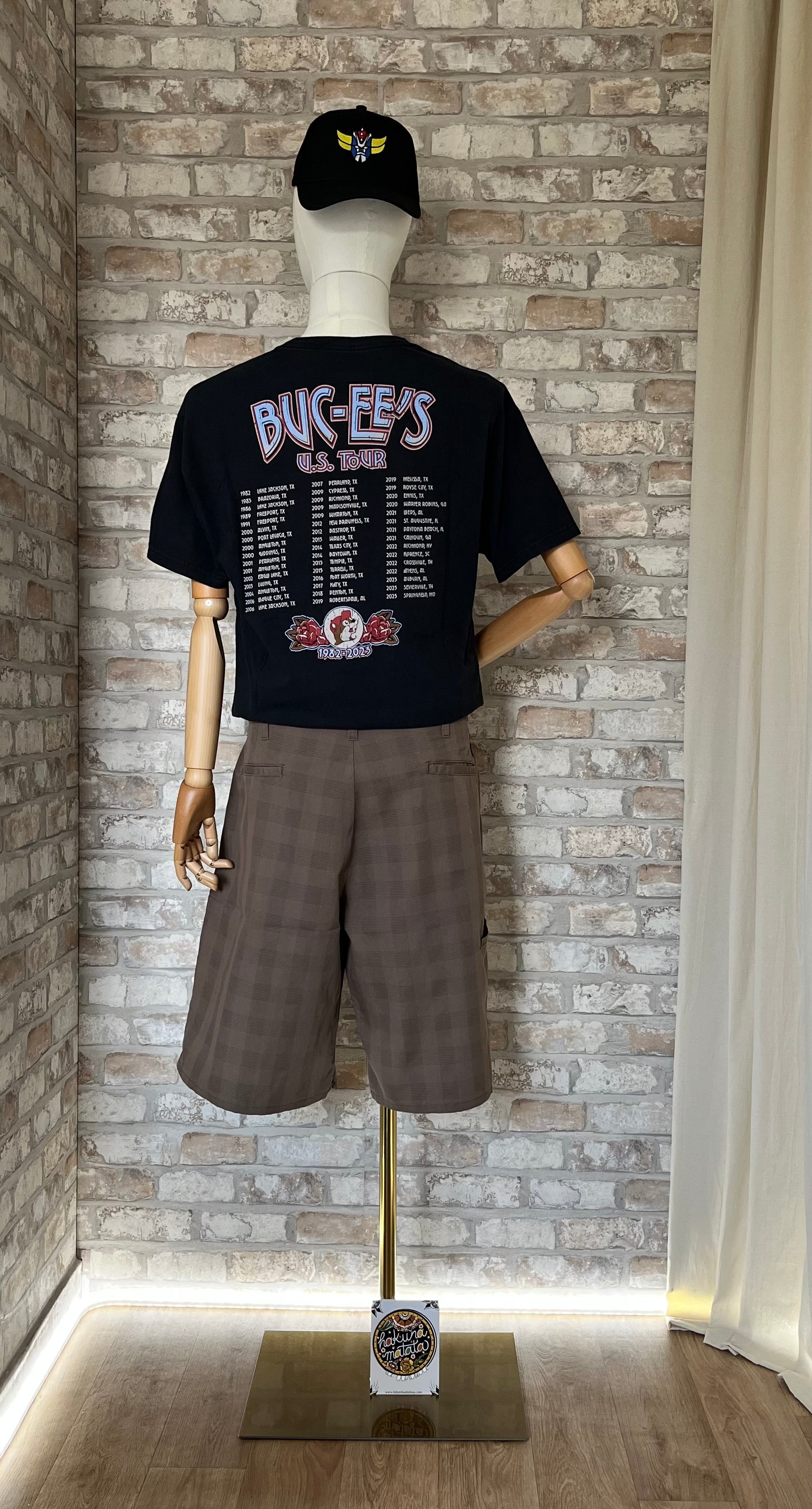 Bermuda Dickies avec T-Shirt Buc-ee'S US Tour Style Rock Band Tee Vintage Import USA de dos sur mannequin avec casquette Goldorak Grafitee et un Patch La Barbuda au sol