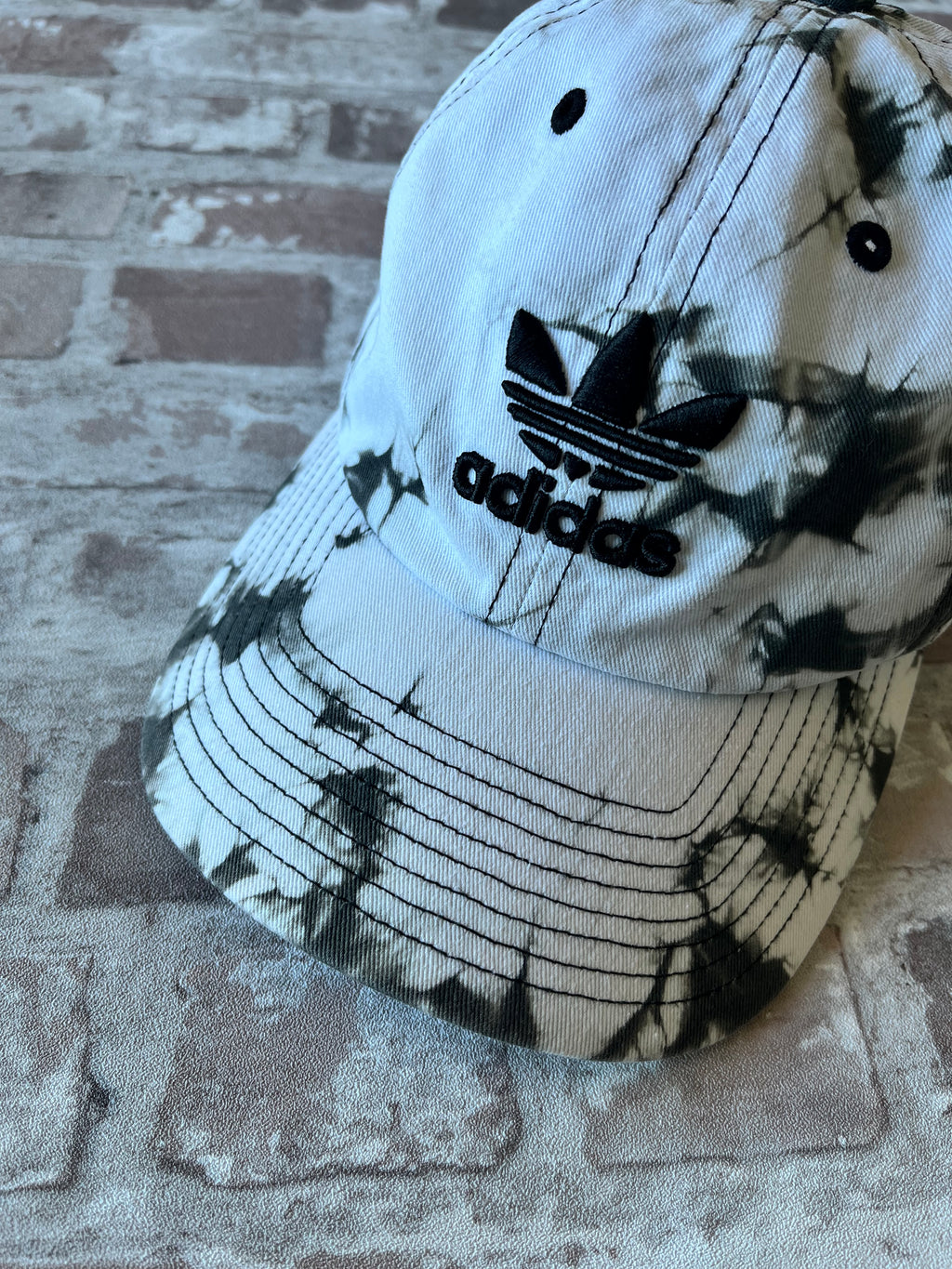 Casquette dad hat Adidas Originals au motif tie-dye marbré noir et blanc avec logo trèfle brodé, présentée à plat.