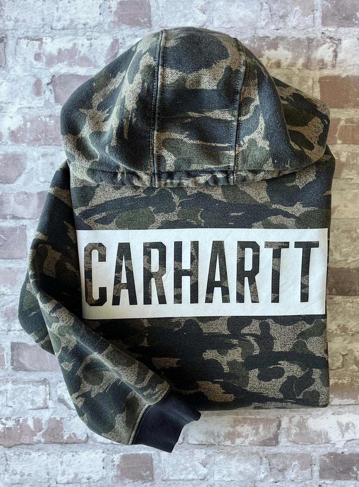 Sweat à capuche vintage Carhartt avec imprimé camouflage kaki et beige, grand logo blanc central sur la poitrine, présenté à plat, plié