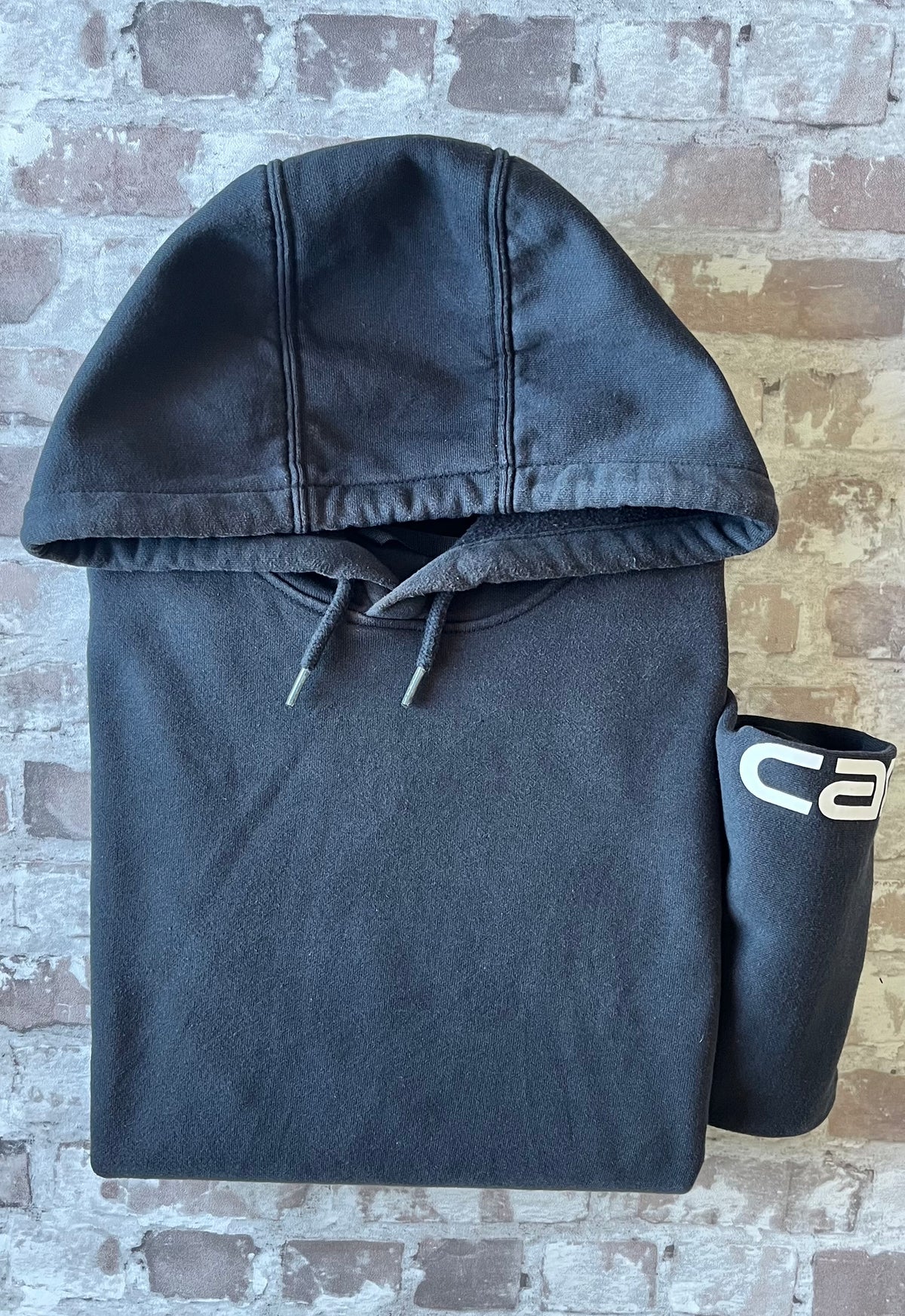 Sweat à capuche noir Carhartt K288 Heavyweight à patine décolorée avec écusson de la marque sur la poche kangourou, présenté à plat, plié