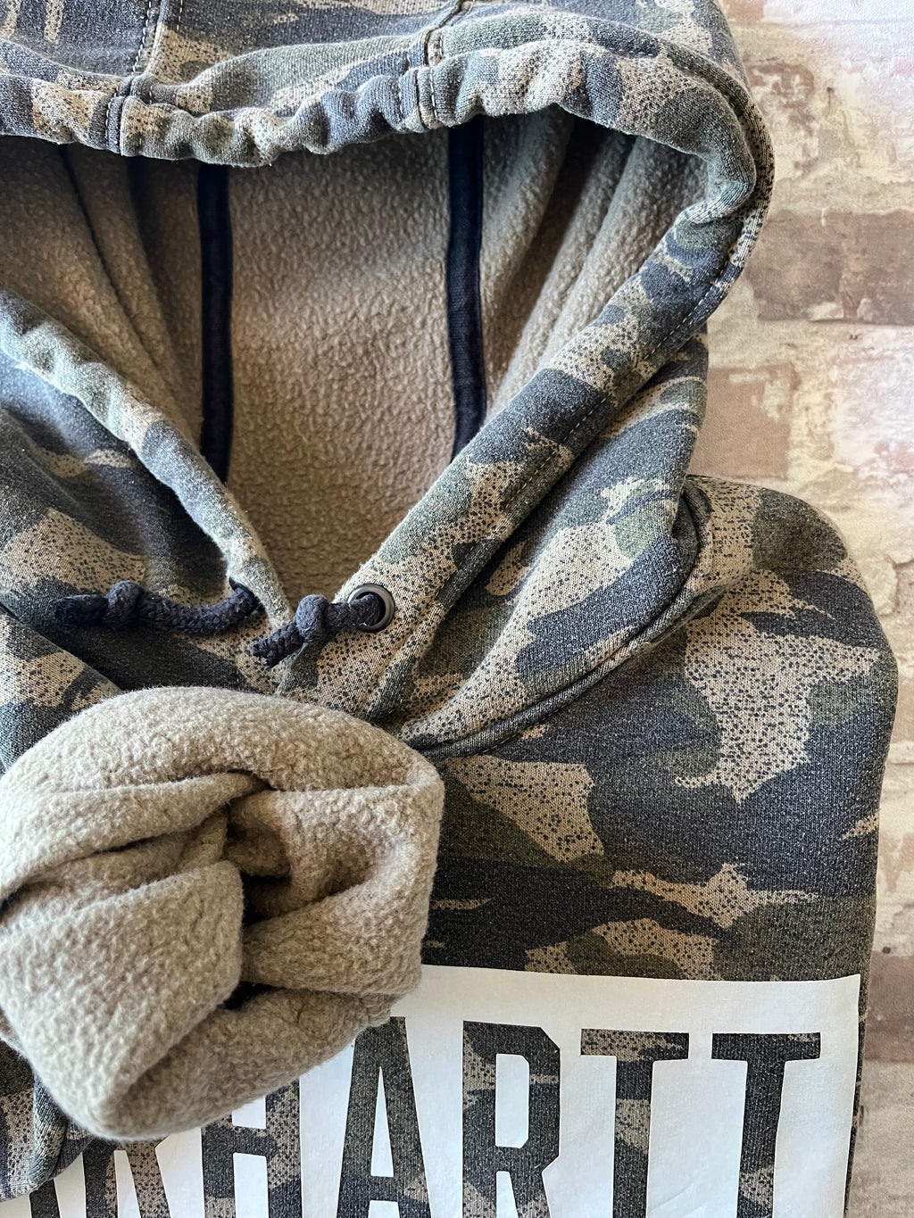 Sweat à capuche vintage Carhartt avec imprimé camouflage kaki et beige, grand logo blanc central sur la poitrine, présenté à plat focus doublure