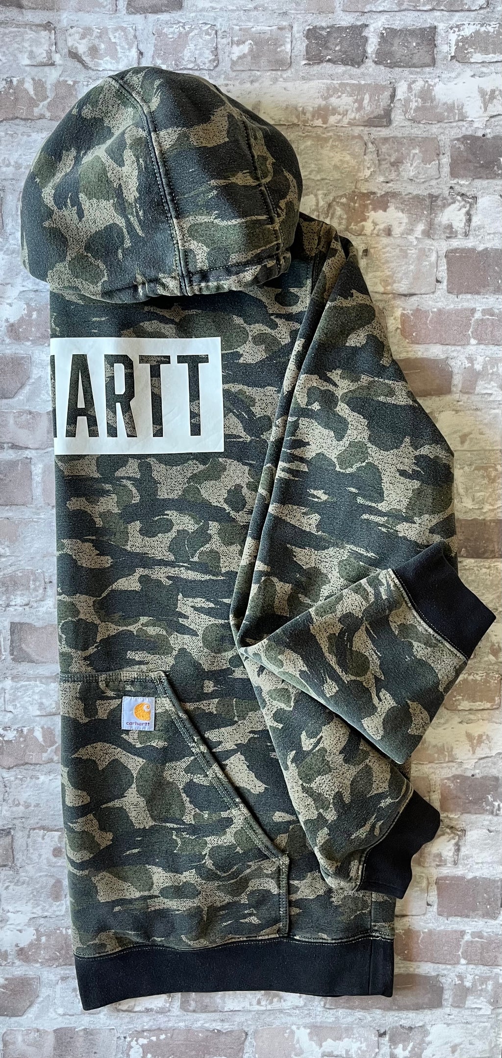 Sweat à capuche vintage Carhartt avec imprimé camouflage kaki et beige, grand logo blanc central sur la poitrine, présenté à plat, profil