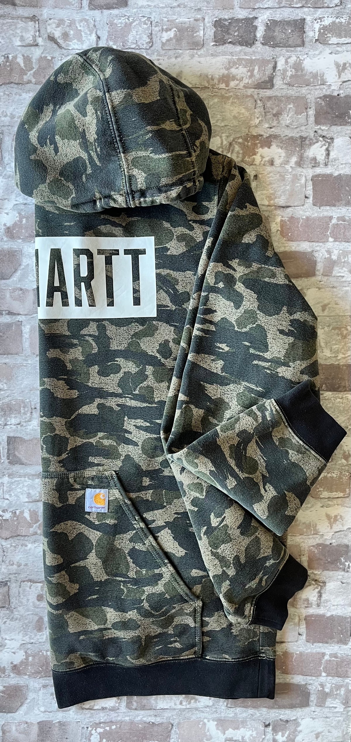 Sweat à capuche vintage Carhartt avec imprimé camouflage kaki et beige, grand logo blanc central sur la poitrine, présenté à plat, profil