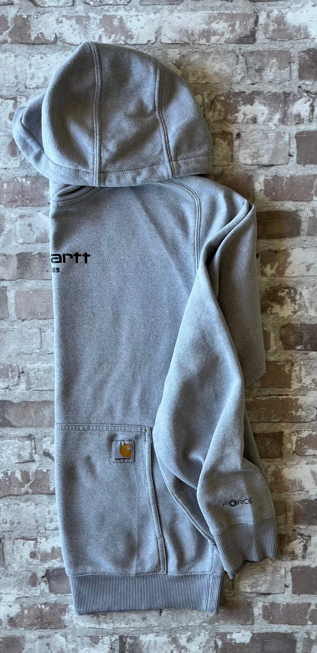 Sweat à capuche vintage Carhartt Force gris clair chiné avec imprimé EST 1889 sur la poitrine et écusson tissé sur la poche, présenté plié à plat, de profil