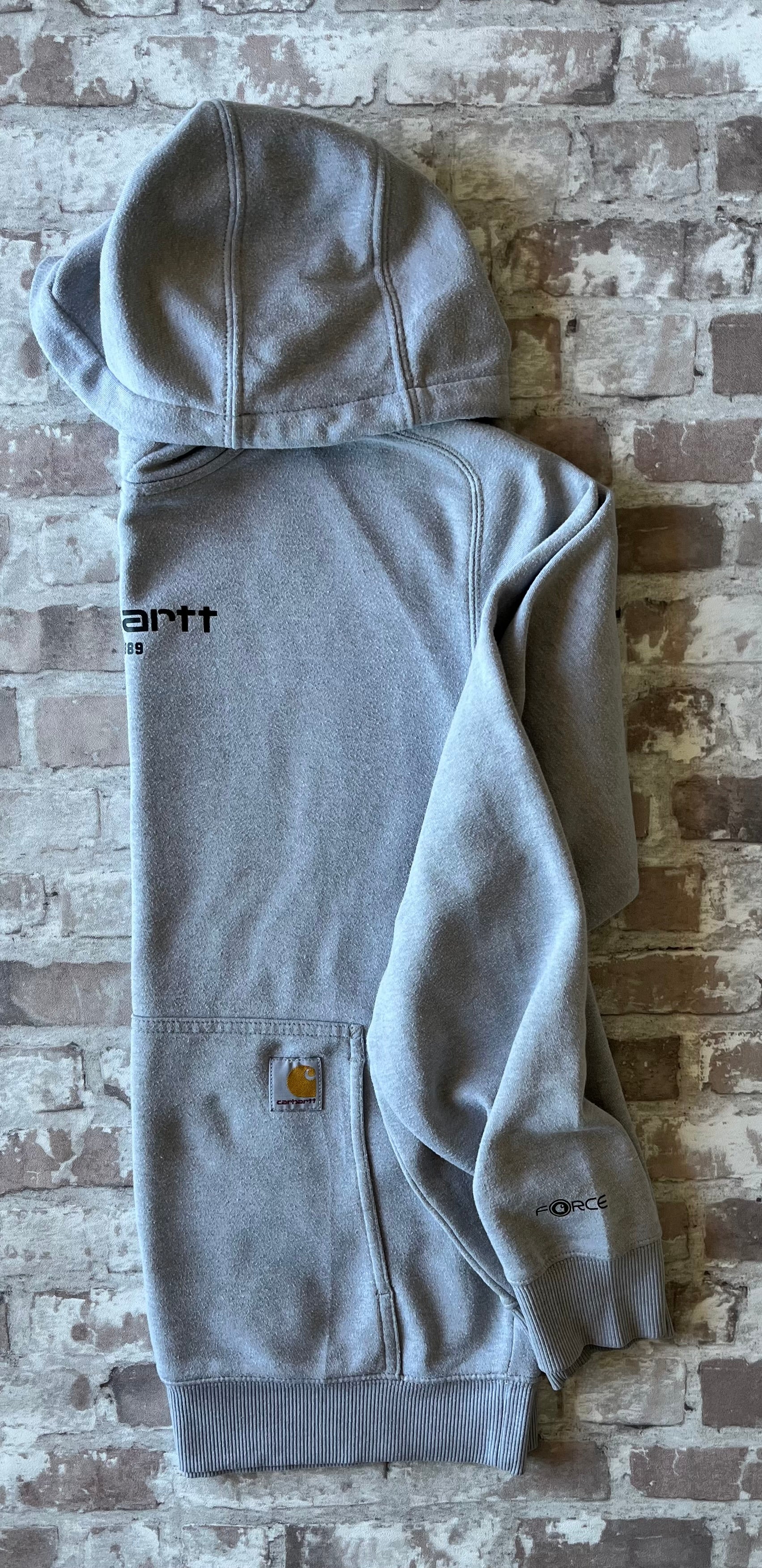 Sweat à capuche vintage Carhartt Force gris clair chiné avec imprimé EST 1889 sur la poitrine et écusson tissé sur la poche, présenté plié à plat, de profil