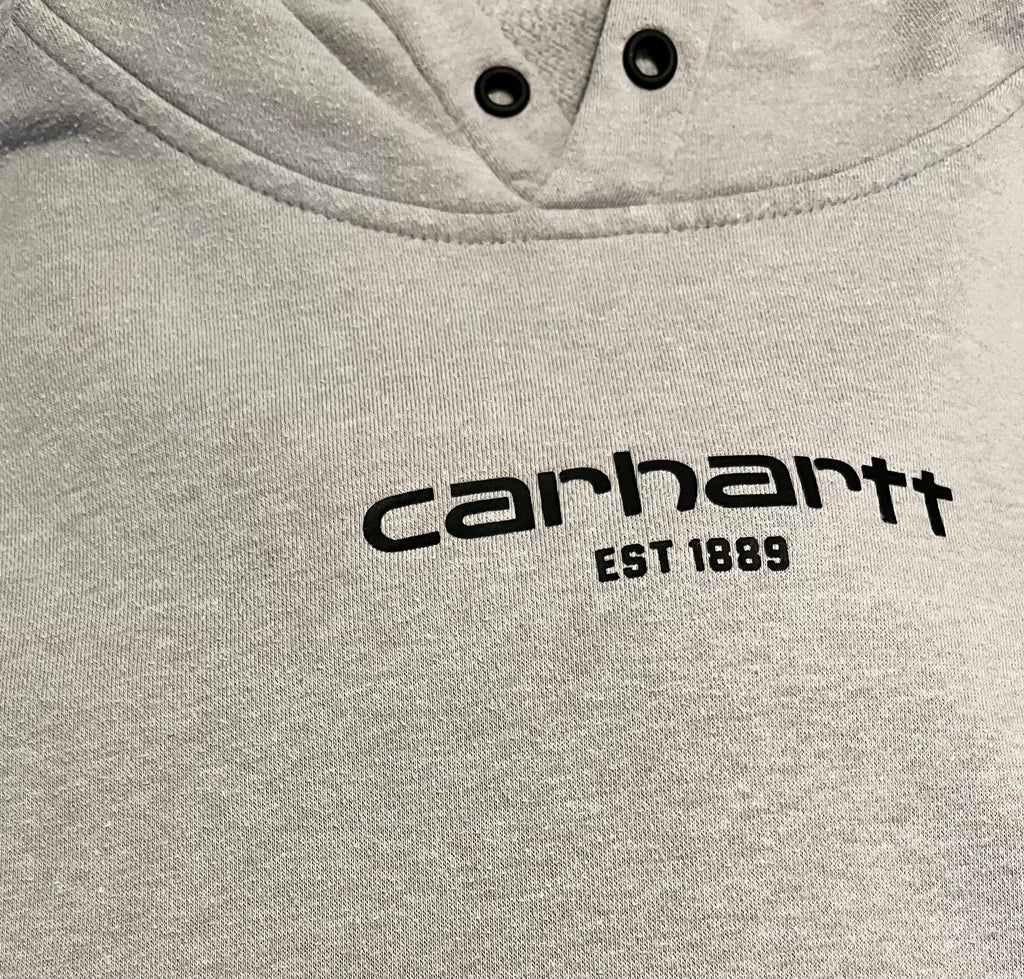 Gros plan sur les légères taches d'usage et la patine du tissu sur le devant d'un hoodie en coton gris Carhartt au style authentique.