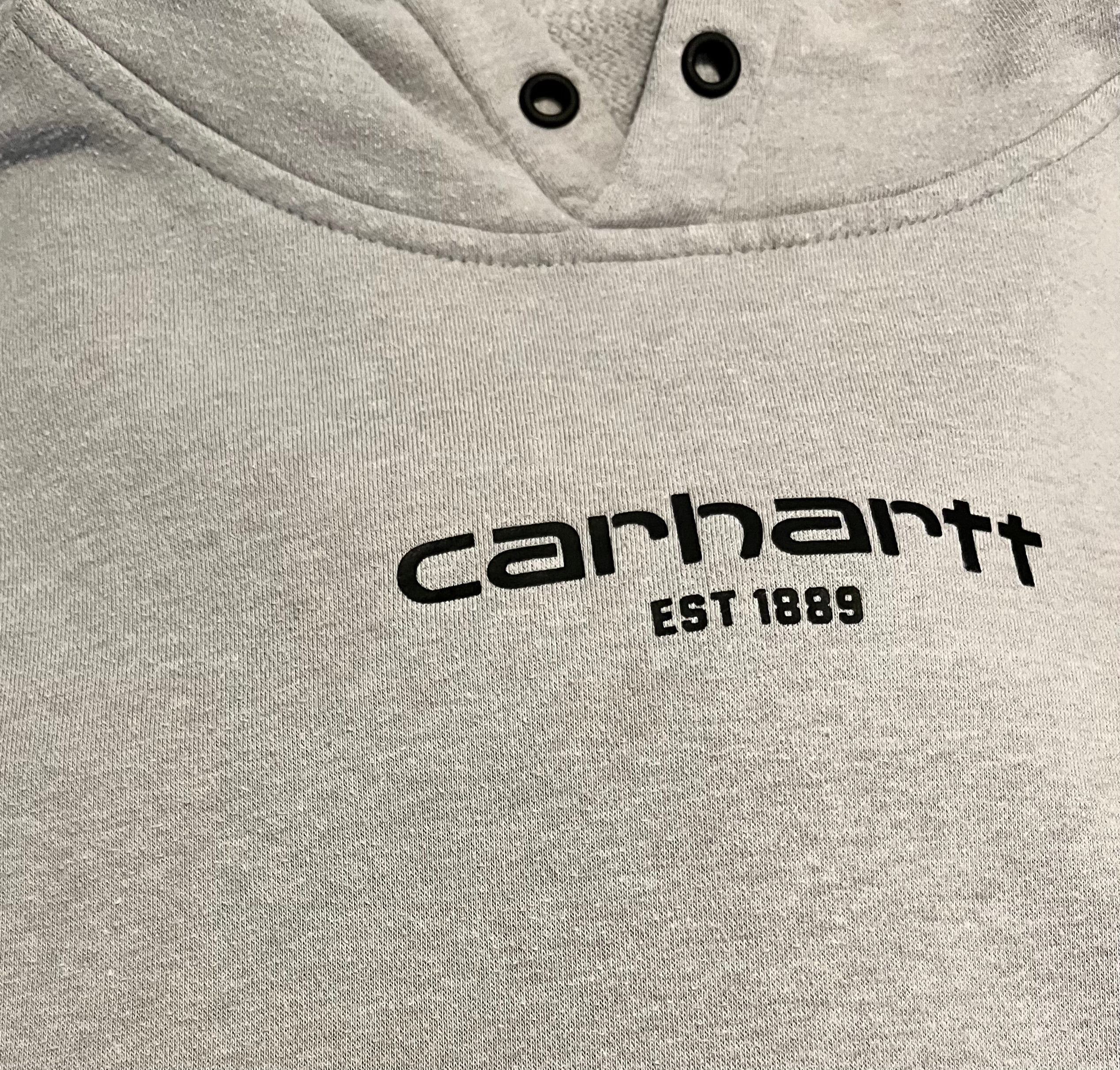 Gros plan sur les légères taches d'usage et la patine du tissu sur le devant d'un hoodie en coton gris Carhartt au style authentique.