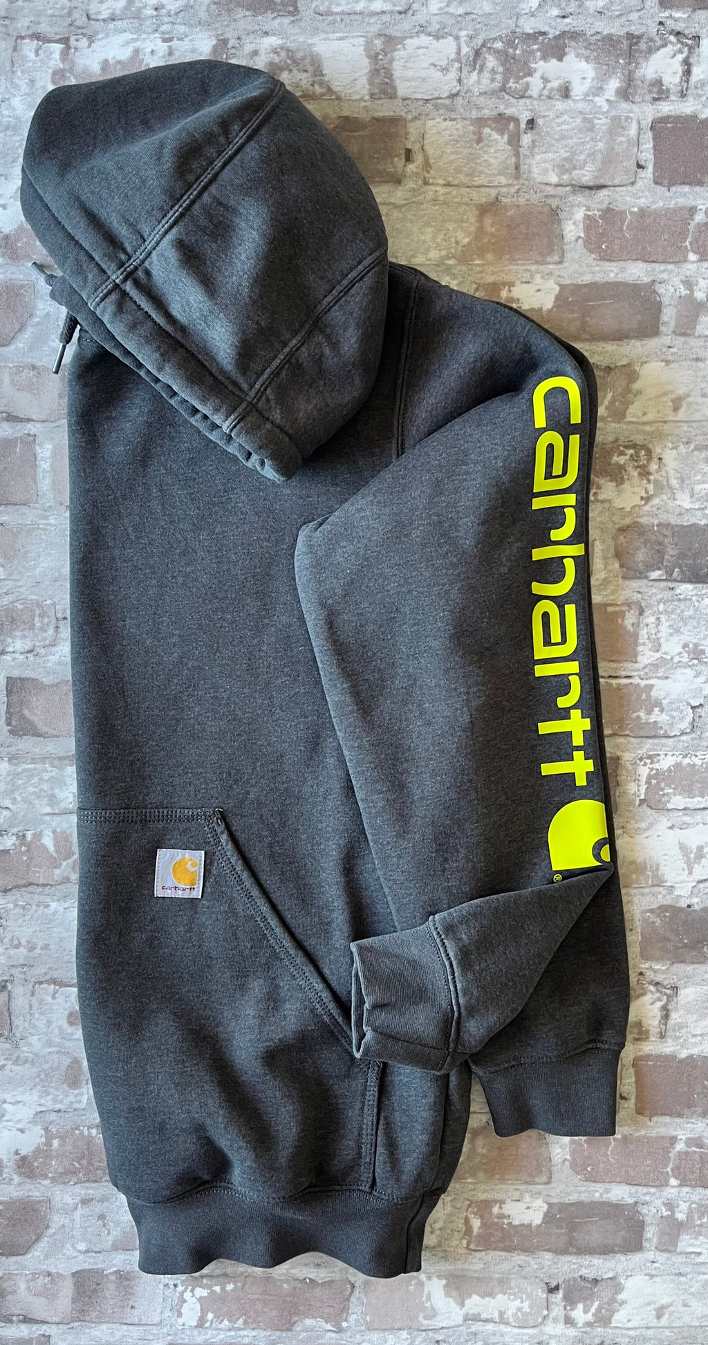 Sweat à capuche vintage Carhartt K288 gris anthracite Carbon Heather avec écusson cousu sur la poche kangourou avant, présenté à plat, de profil