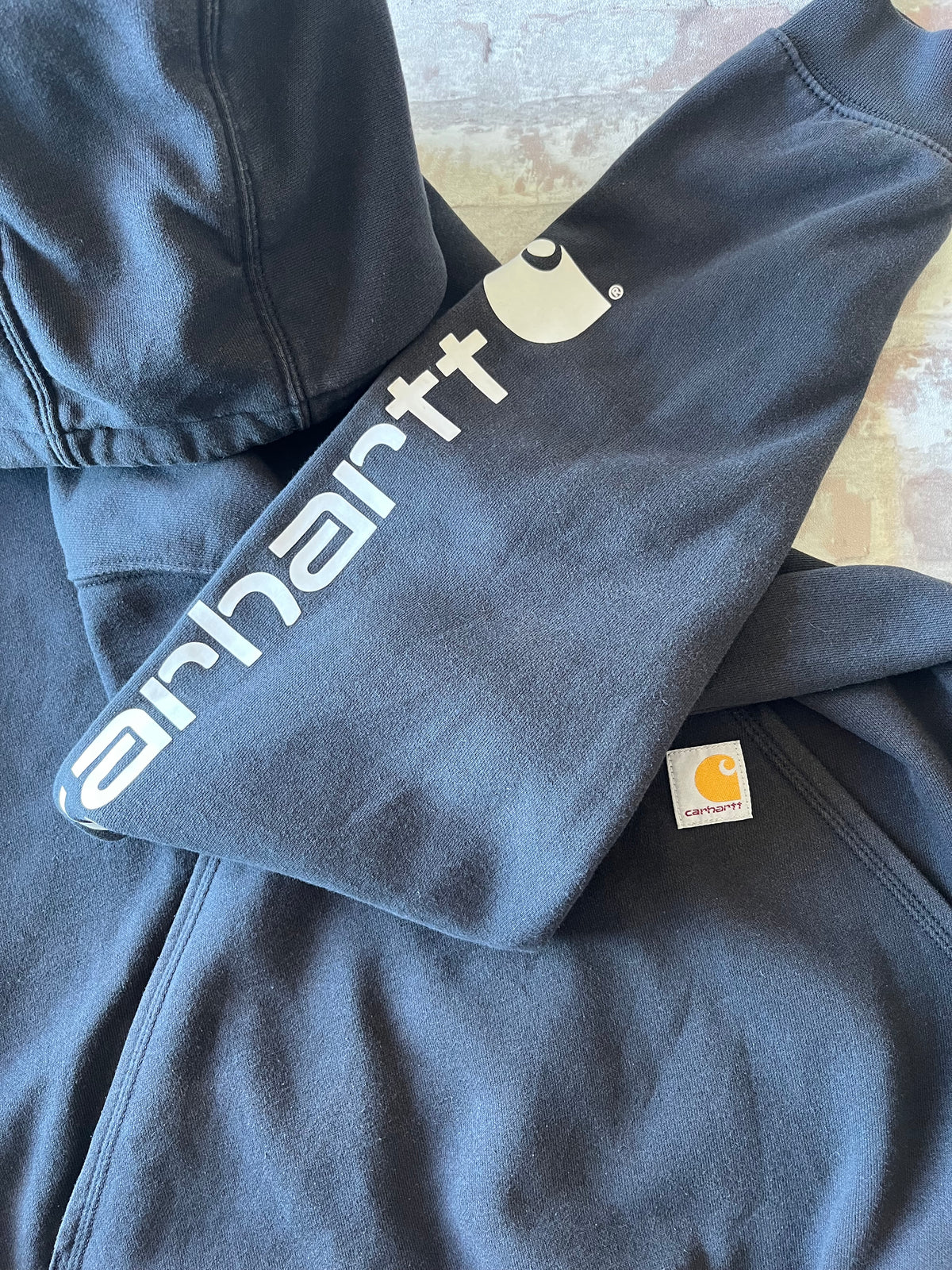 Gros plan sur le logo textuel blanc Carhartt imprimé le long de la manche gauche d'un hoodie en coton épais noir.