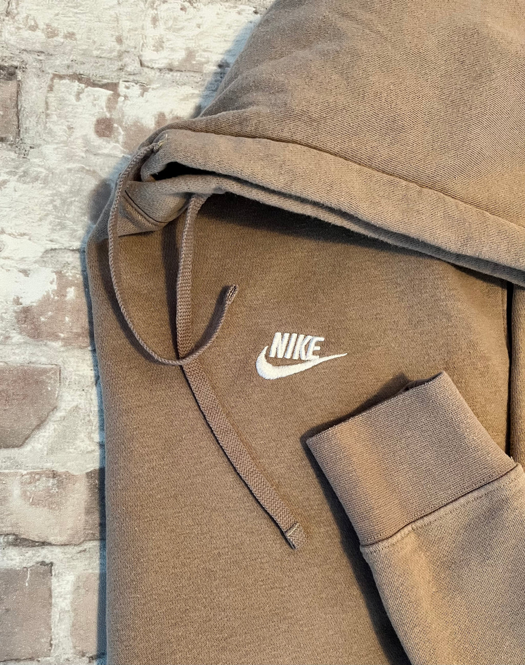 Sweat à capuche Nike Club Fleece couleur beige sable clair avec logo Futura brodé sur la poitrine, présenté plié à plat.
