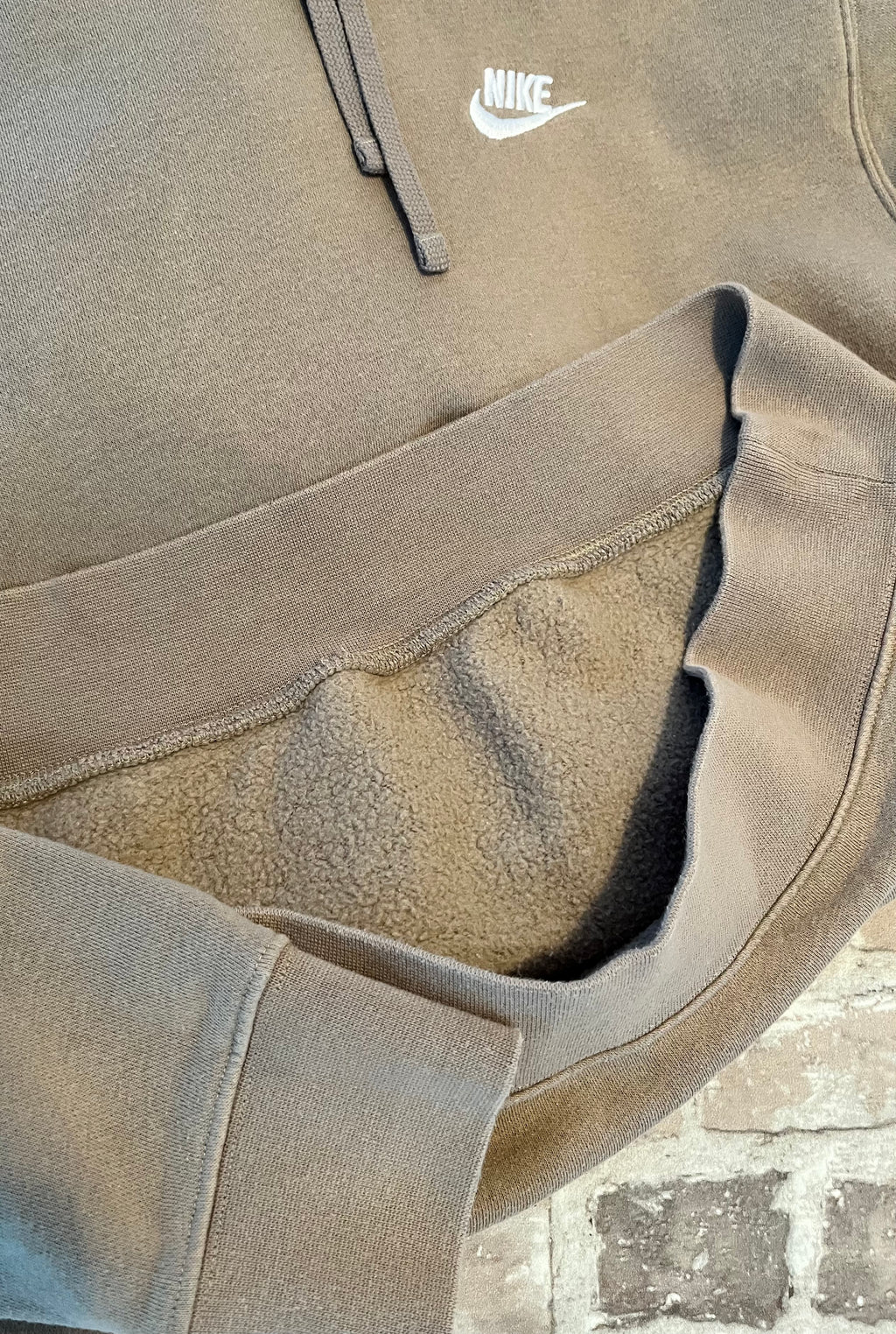 Sweat à capuche Nike Club Fleece couleur beige sable clair avec logo Futura brodé sur la poitrine, présenté plié à plat. Focus Doublure