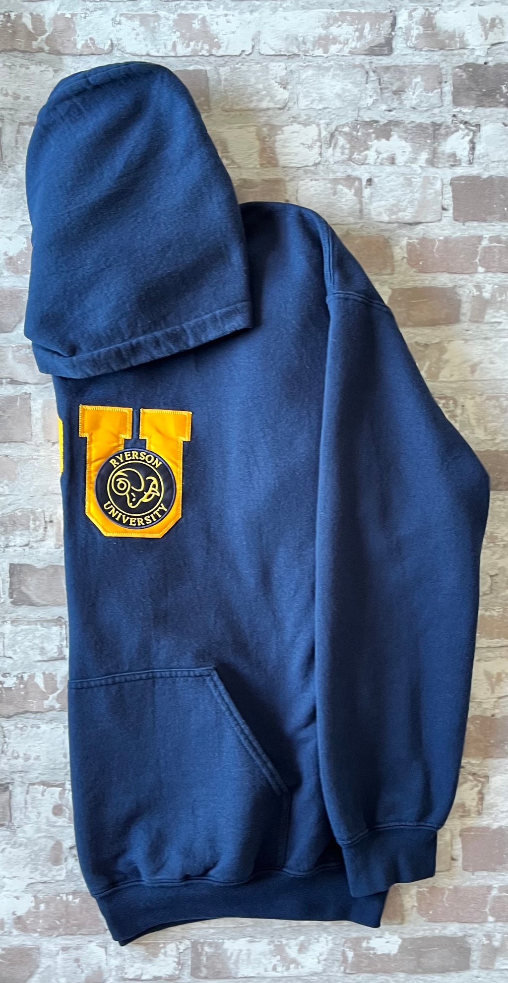 Sweat à capuche vintage bleu marine Ryerson Rams avec écusson bélier brodé et grand lettrage RU en satin jaune, présenté plié à plat, de profil