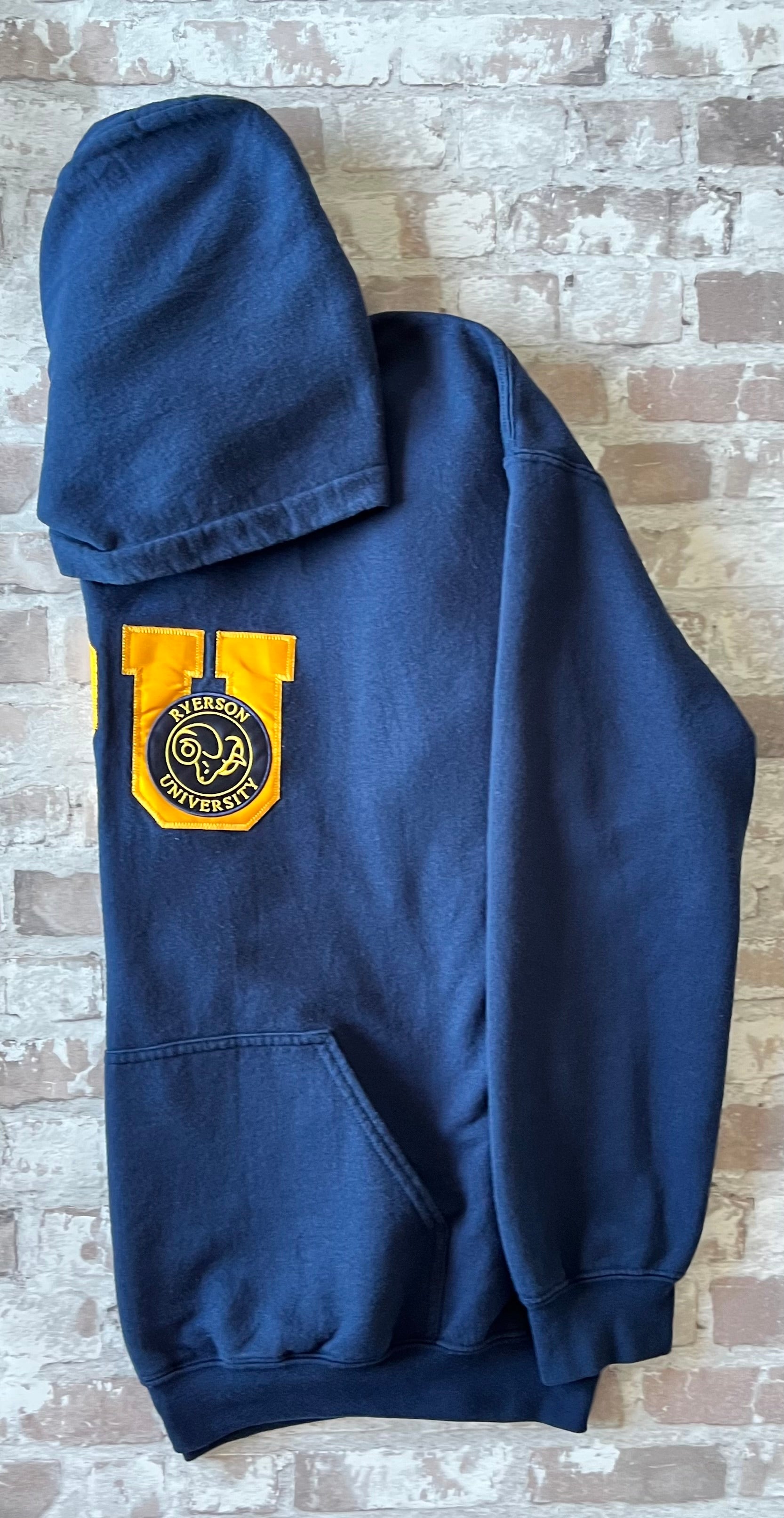 Sweat à capuche vintage bleu marine Ryerson Rams avec écusson bélier brodé et grand lettrage RU en satin jaune, présenté plié à plat, de profil