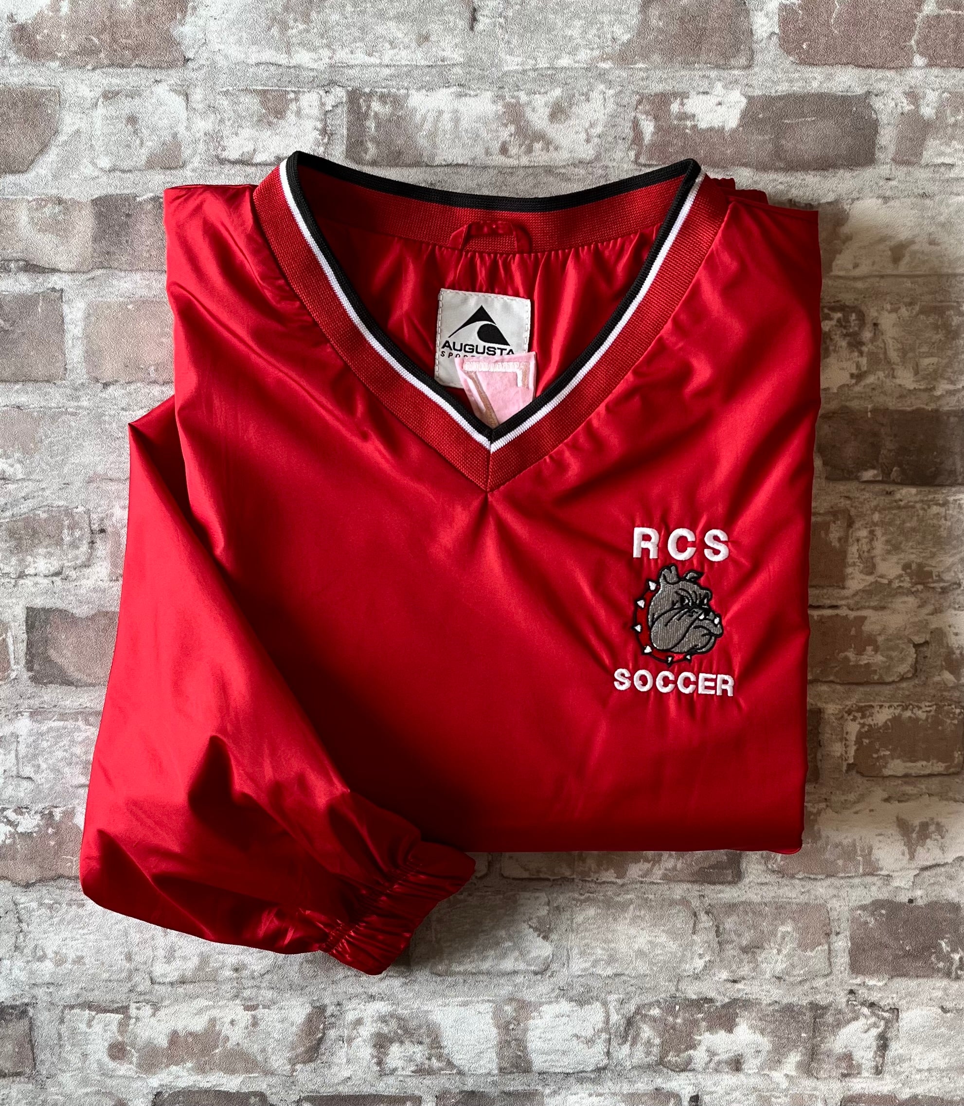 Veste de sport pullover rétro Augusta Sportswear rouge vif avec col en V en maille et logo Bulldog brodé, présentée pliée à plat.