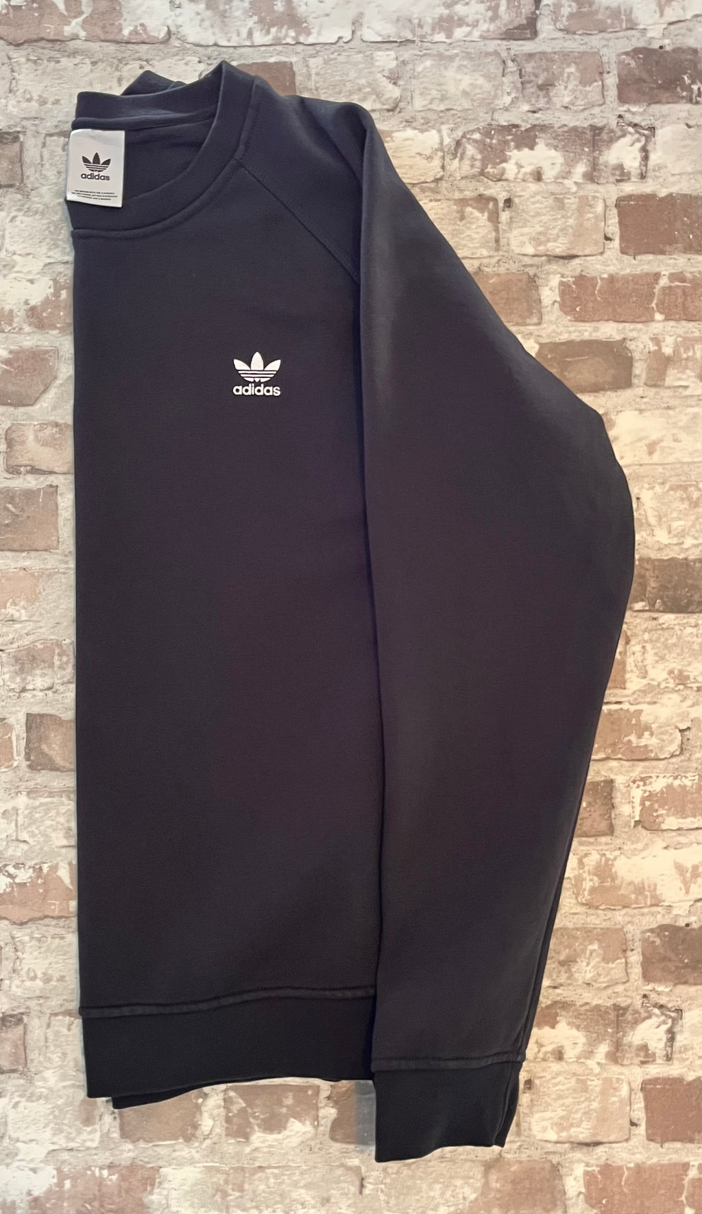 Sweat col rond vintage Adidas Originals noir avec l'iconique logo trèfle blanc brodé sur la poitrine, présenté plié à plat, de profil