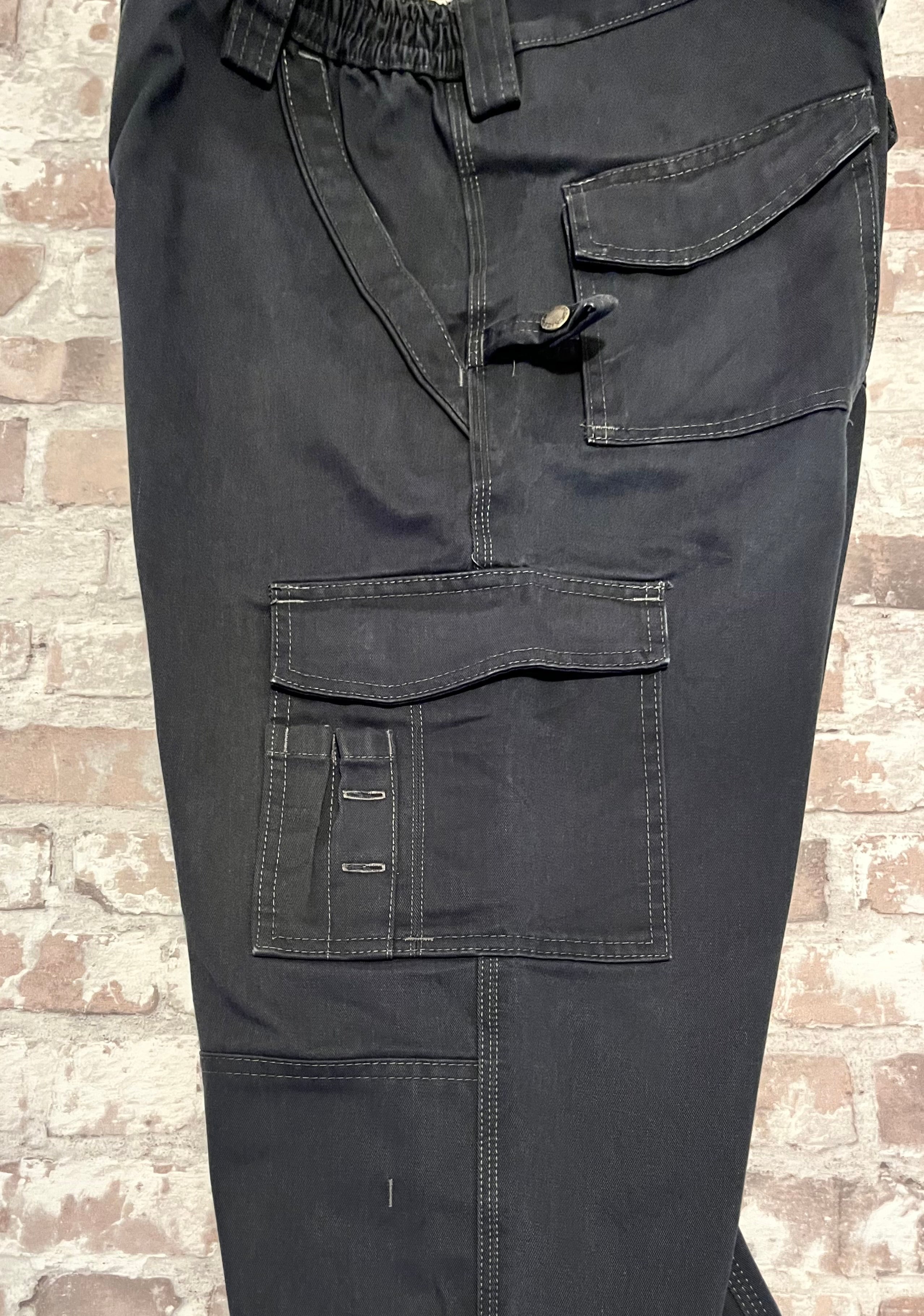 Gros plan sur la ceinture élastique, la boucle à outils et le patch logo tissé d'un pantalon cargo noir Dickies.