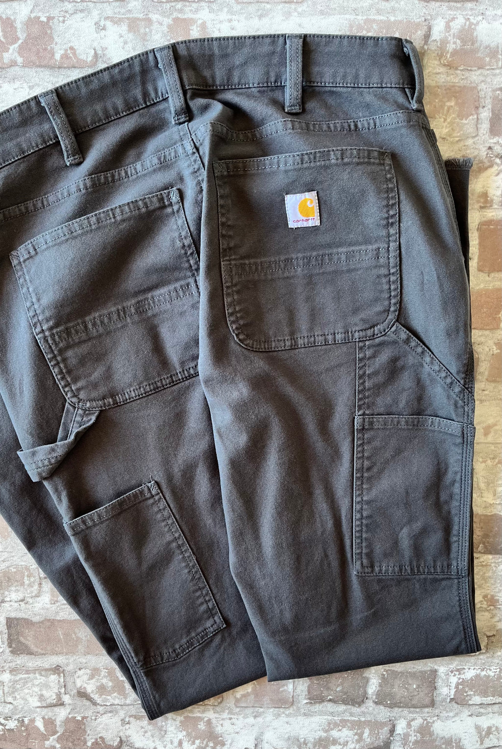 Pantalon de travail gris anthracite femme Carhartt Carpenter avec bas de jambes coupés à cru, présenté à plat, plié et de dos