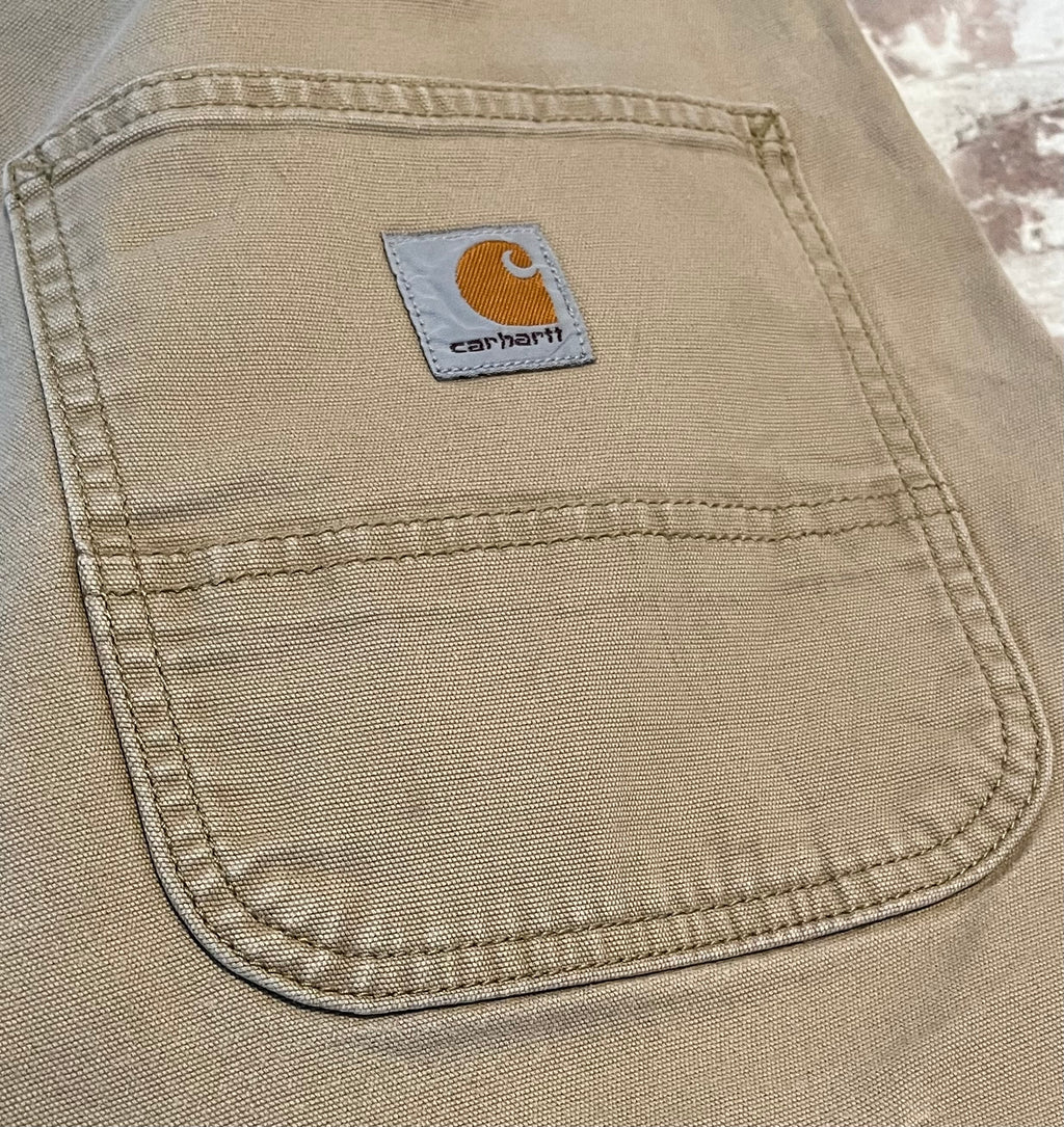 Gros plan sur le patch logo en tissu et les légères marques d'usage sur la poche arrière d'un pantalon Carhartt beige.