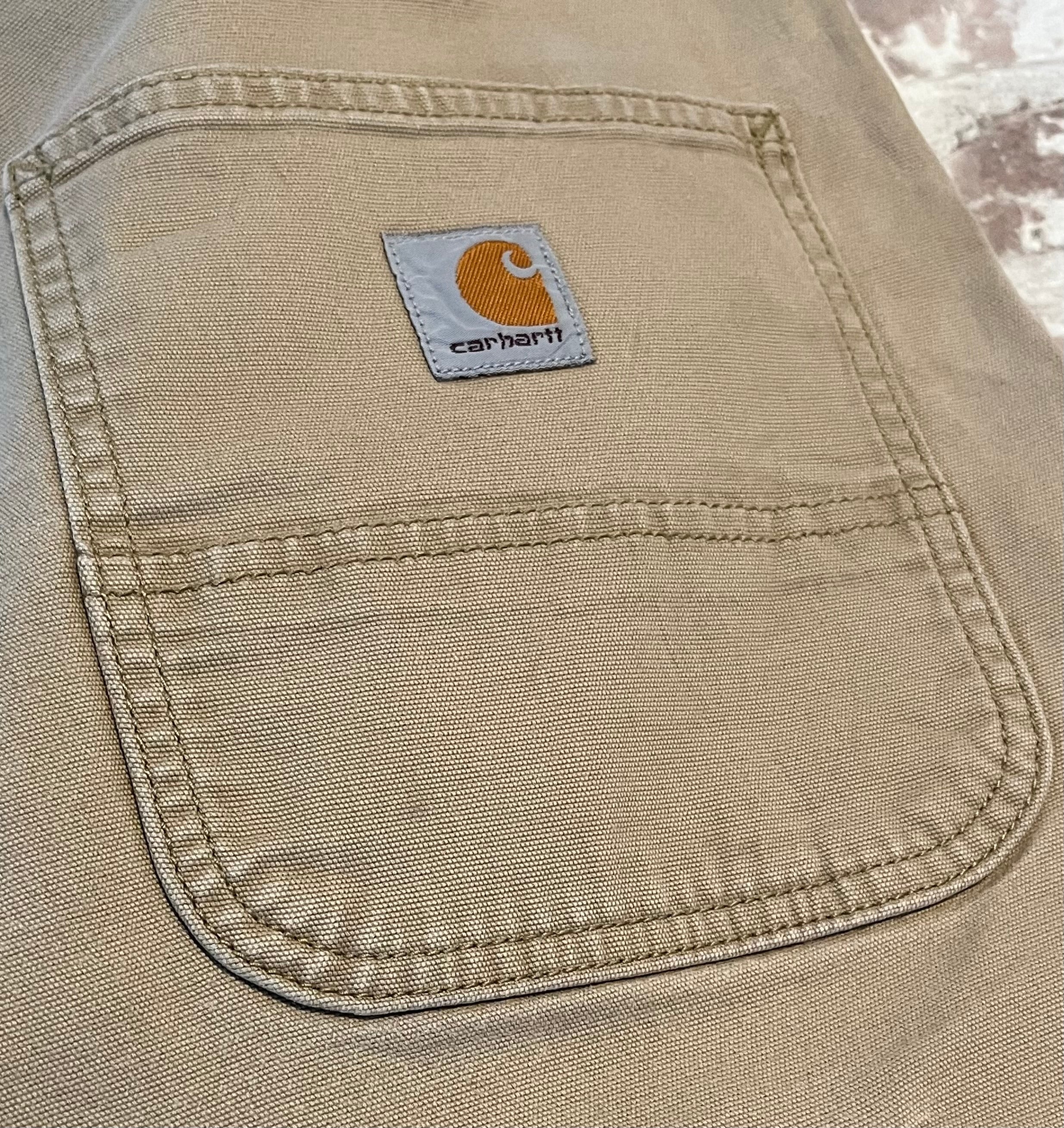 Gros plan sur le patch logo en tissu et les légères marques d'usage sur la poche arrière d'un pantalon Carhartt beige.