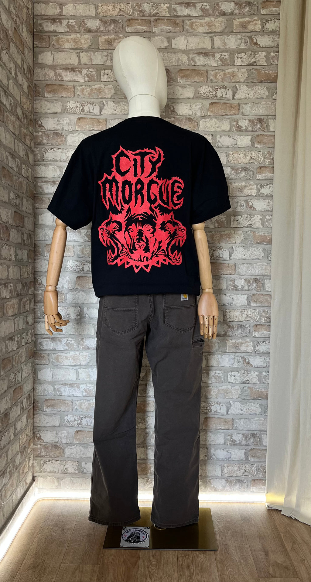 Pantalon Carhartt Relaxed Fit  "5 Pocket" Rugged FlexⓇ coloris Dark Brown avec un tshirt City Morgue porté par un mannequin de dos et un Patch La Barbuda posé au sol