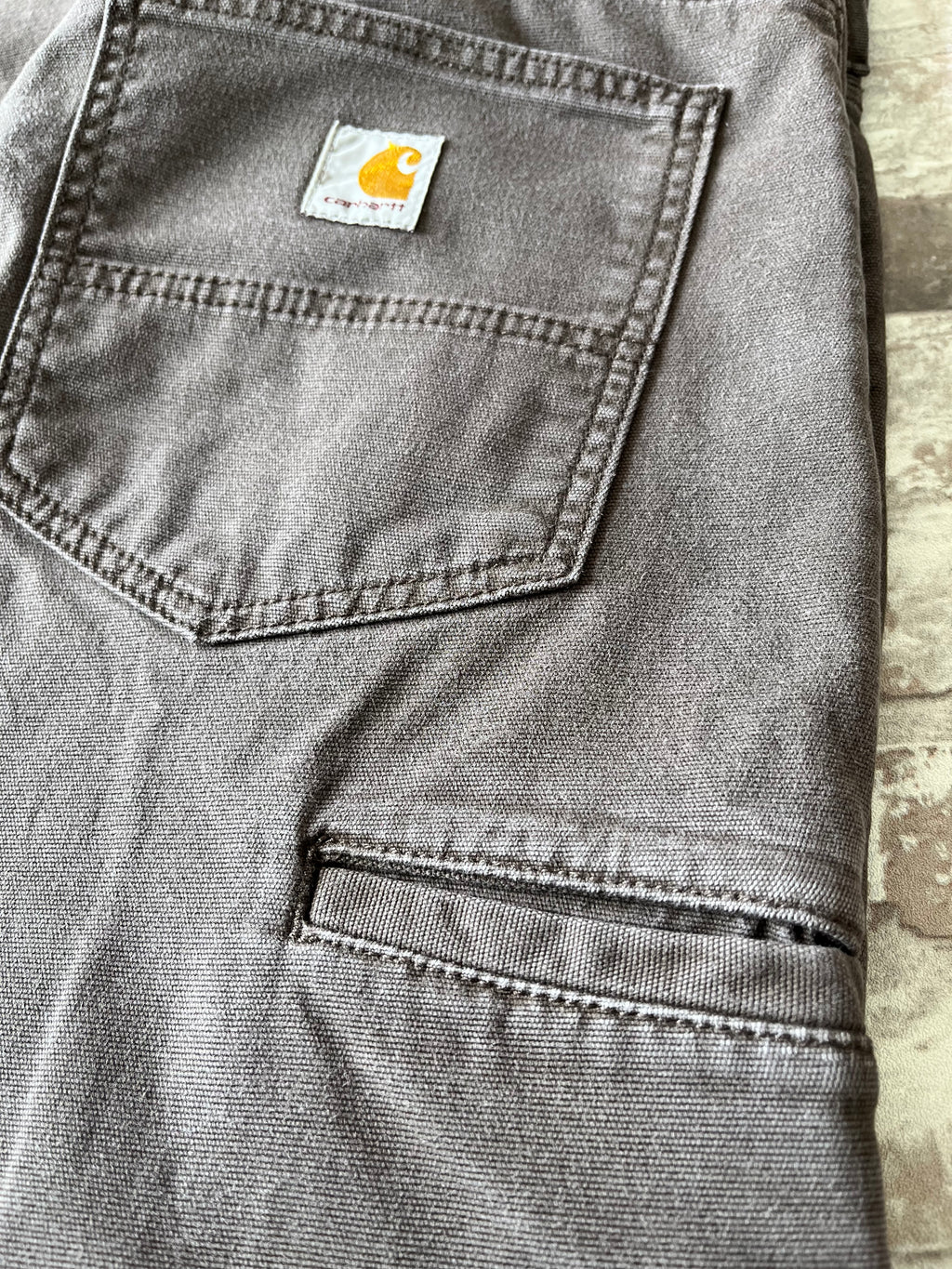 Gros plan sur une poche et le patch logo Carhartt en tissu cousu sur la poche arrière renforcée d'un pantalon marron.