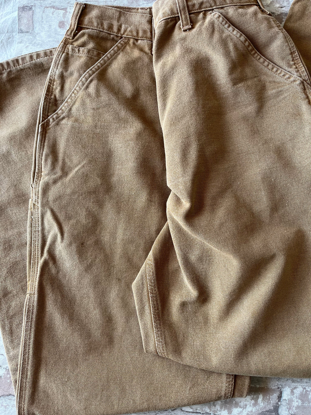 Gros plan sur le bas d'un pantalon Carhartt marron affichant un délavage marbré et des taches de peinture blanche.