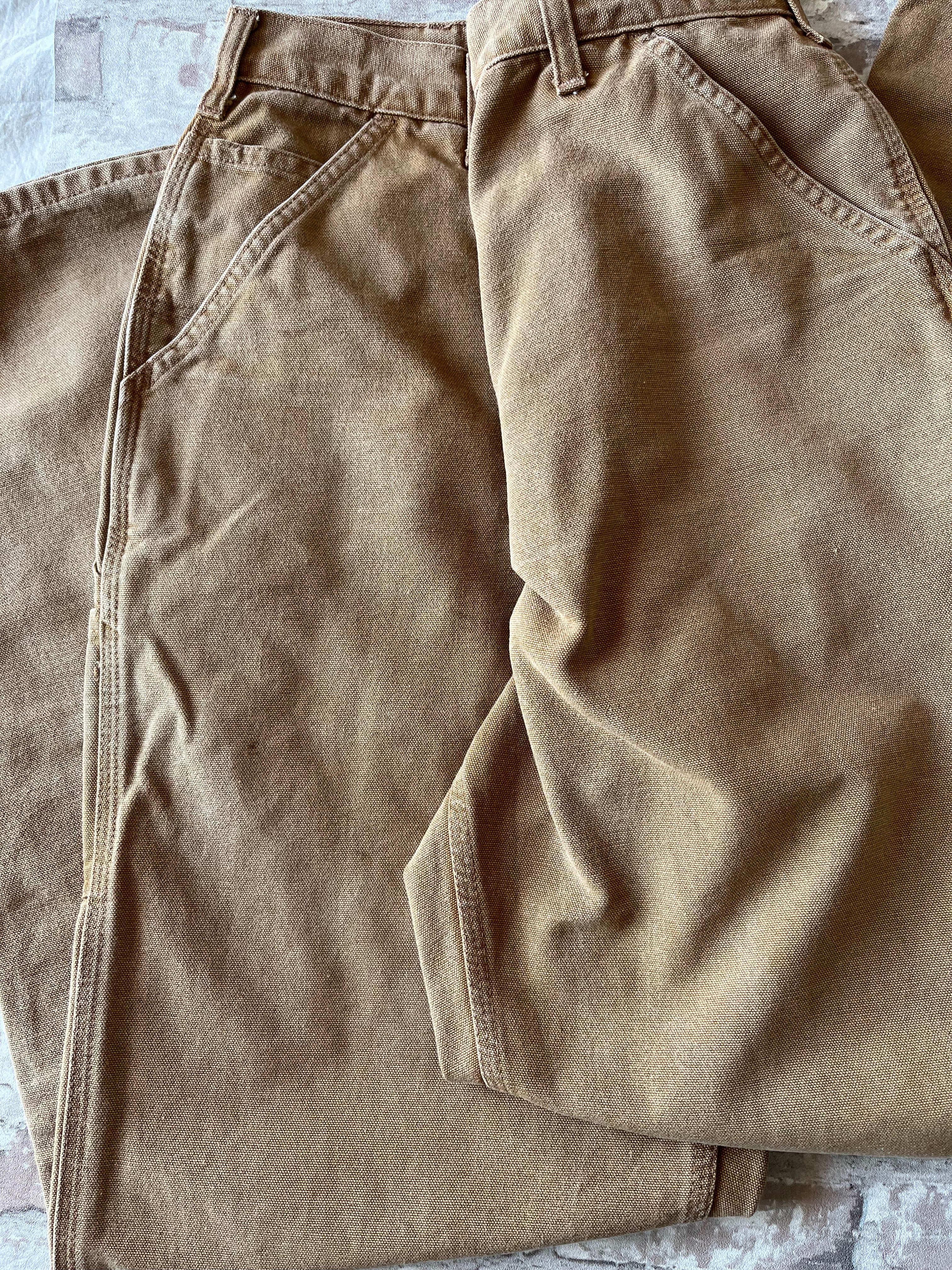 Gros plan sur le bas d'un pantalon Carhartt marron affichant un délavage marbré et des taches de peinture blanche.