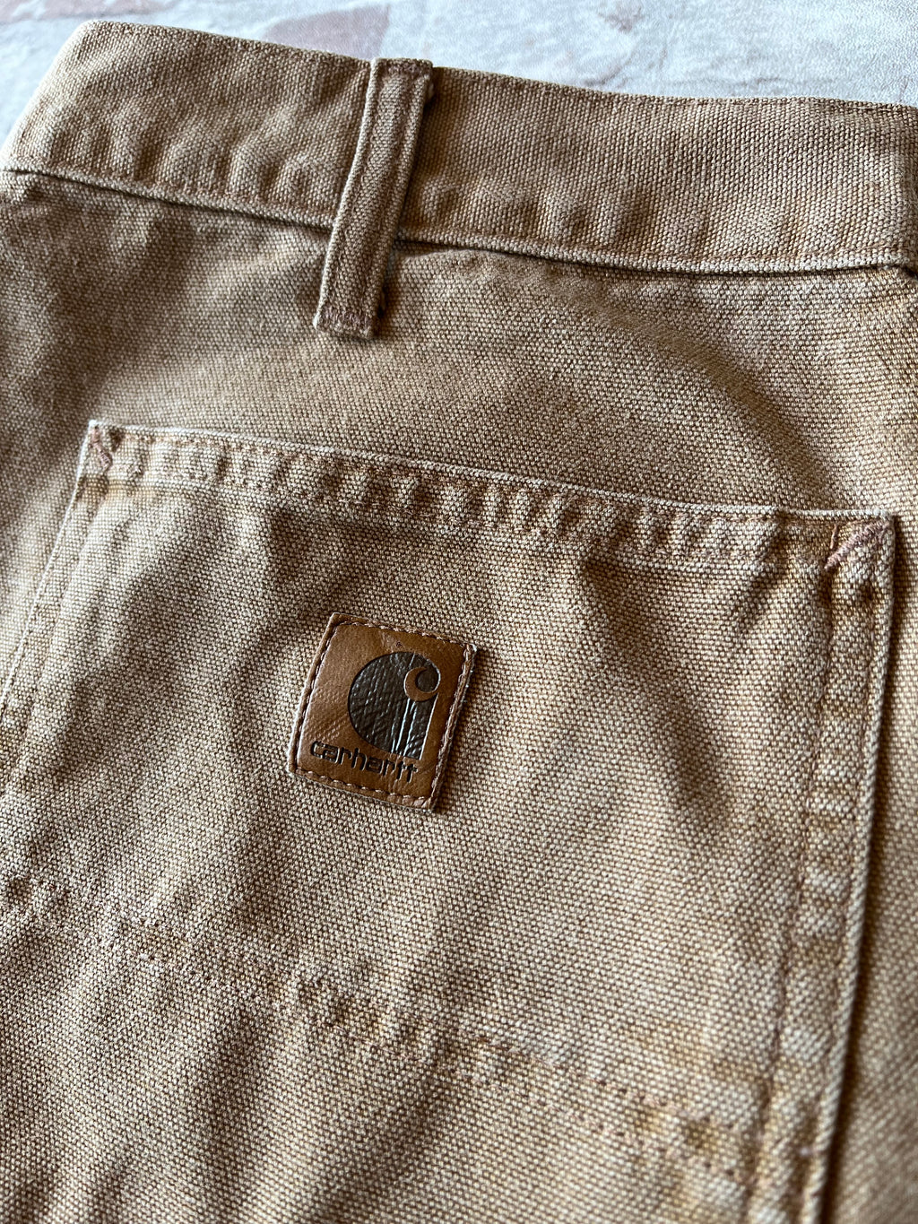 Gros plan sur le patch logo Carhartt en cuir véritable patiné cousu sur la poche arrière d'un pantalon carpenter.