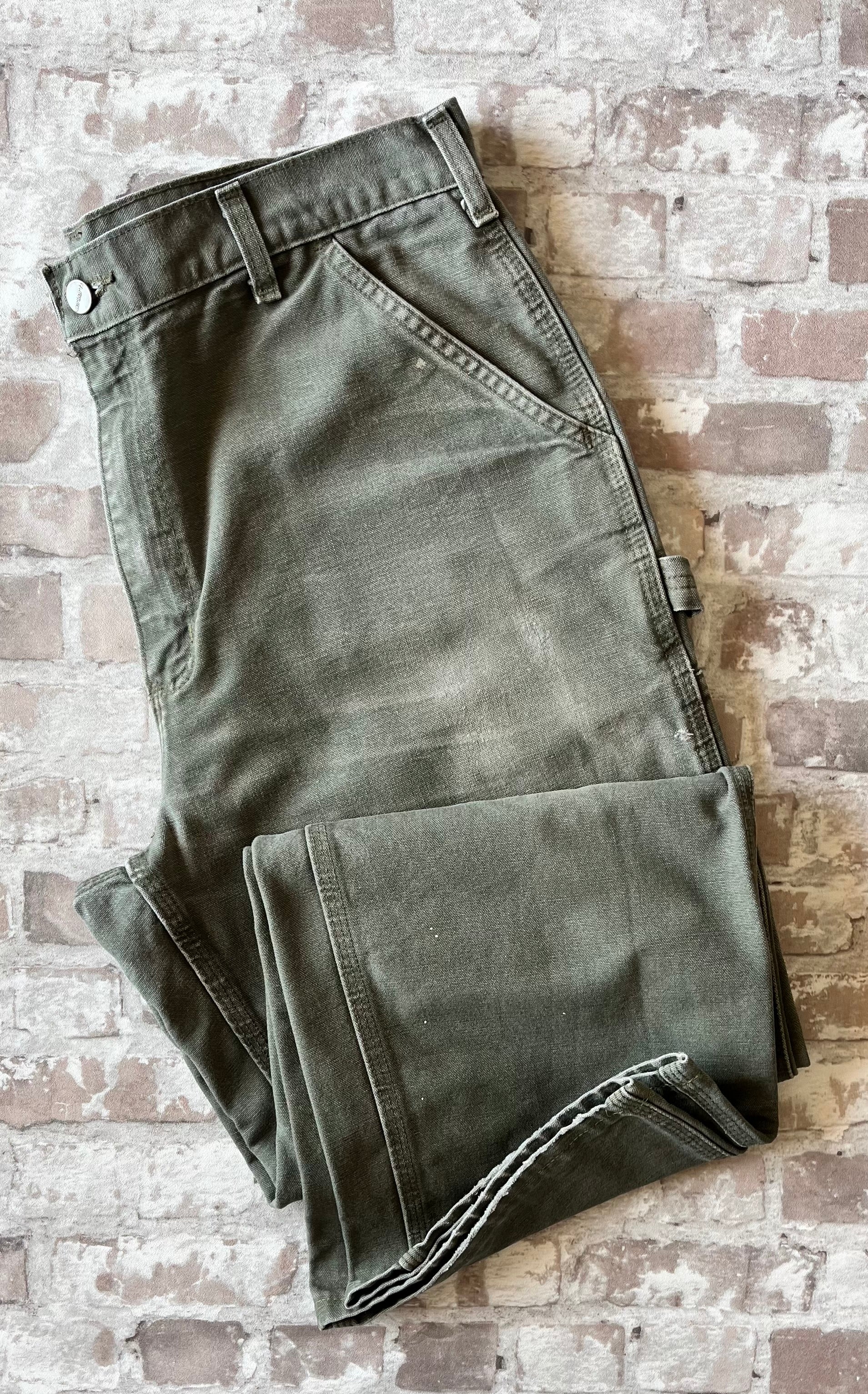 Pantalon de travail vert Moss Carhartt B11 plié à plat, mettant en avant la toile Duck Canvas lourde 