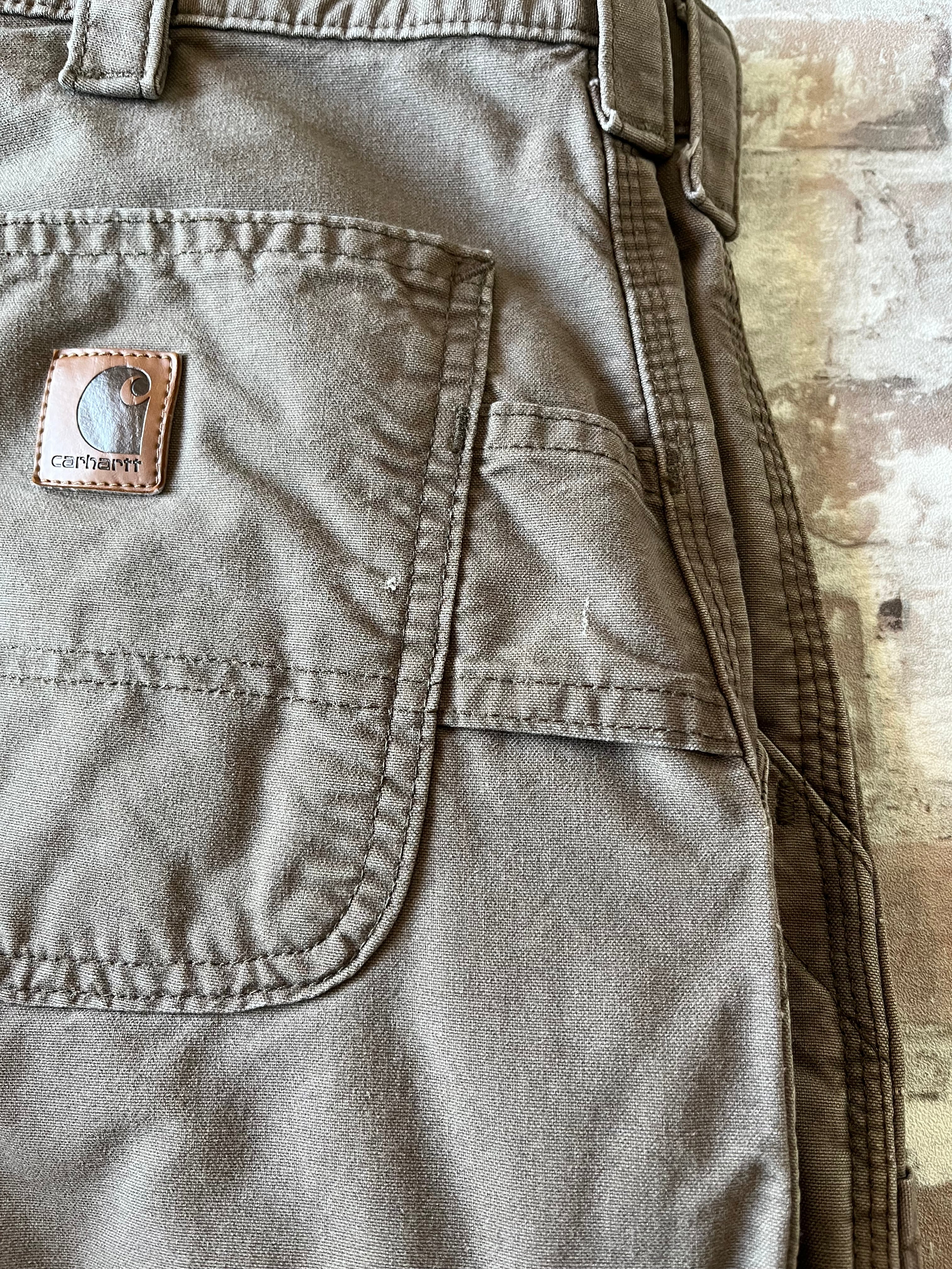 Gros plan sur le patch logo Carhartt en cuir véritable patiné cousu sur la poche arrière renforcée d'un pantalon marron, léger accroc