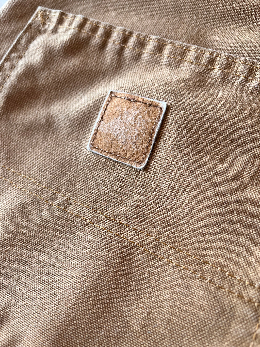 Gros plan sur la poche arrière d'un pantalon Carhartt montrant l'empreinte textile laissée par l'ancien logo disparu.