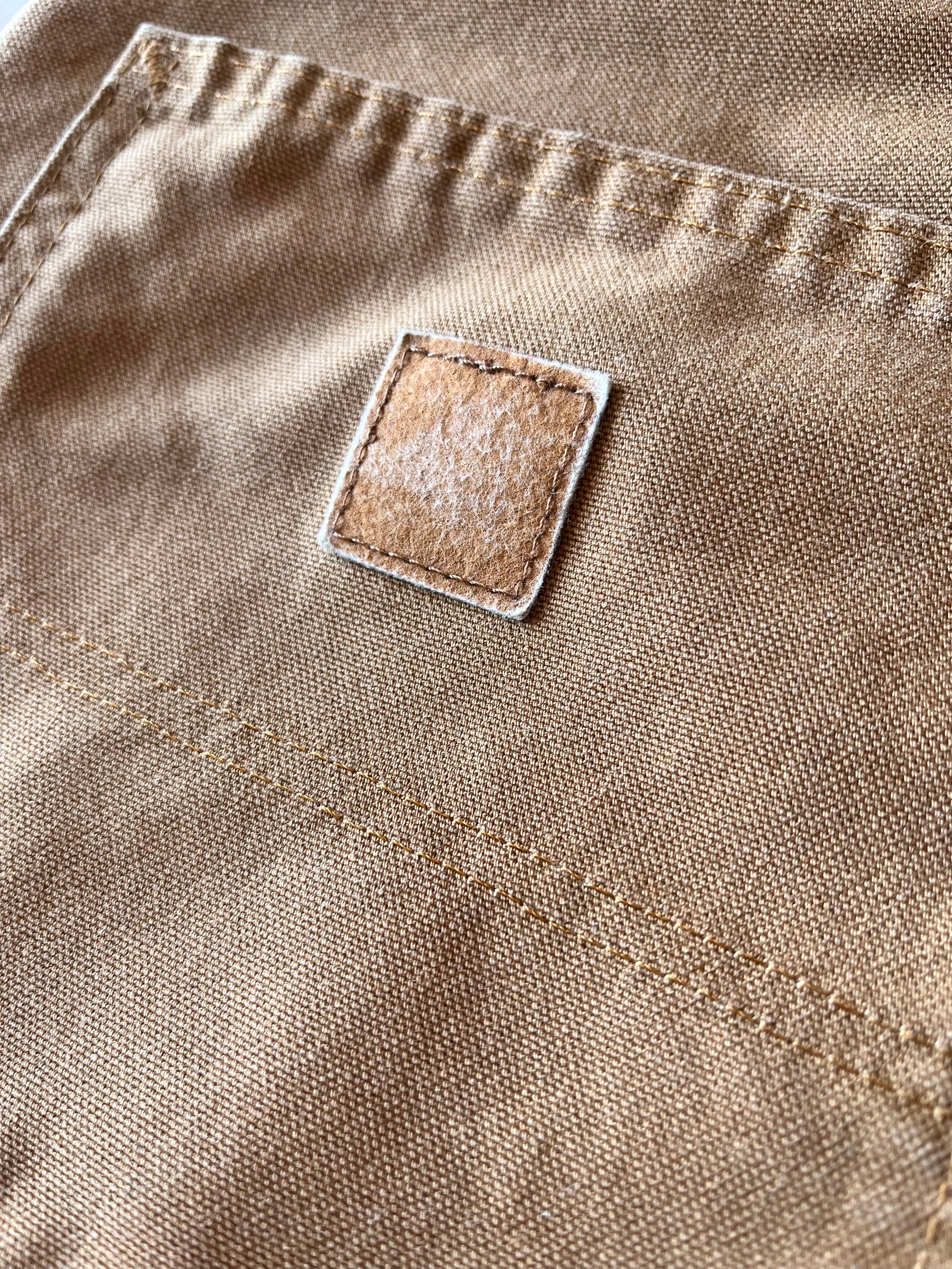 Gros plan sur la poche arrière d'un pantalon Carhartt montrant l'empreinte textile laissée par l'ancien logo disparu.