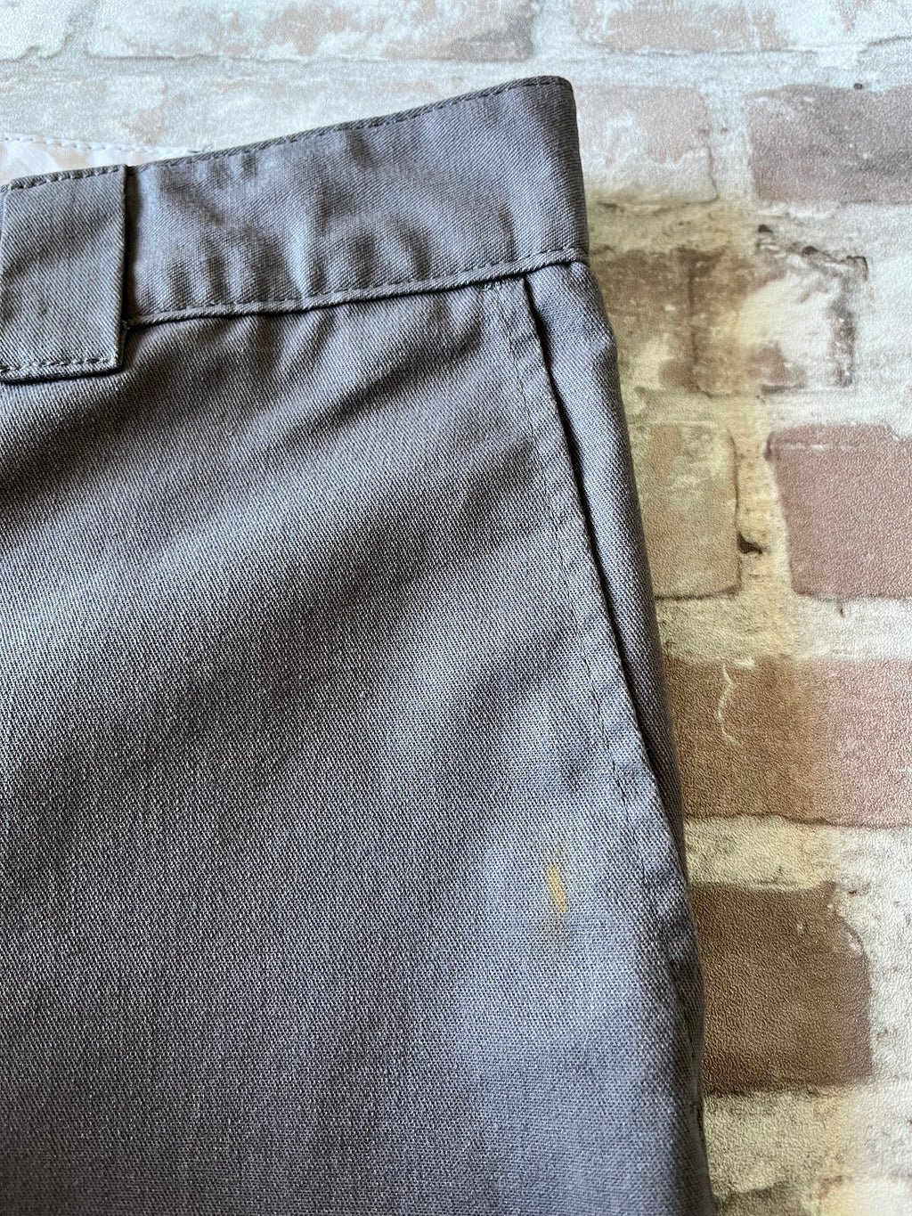 Gros plan sur une tache de peinture dorée unique sur la jambe d'un short Dickies gris de seconde main.