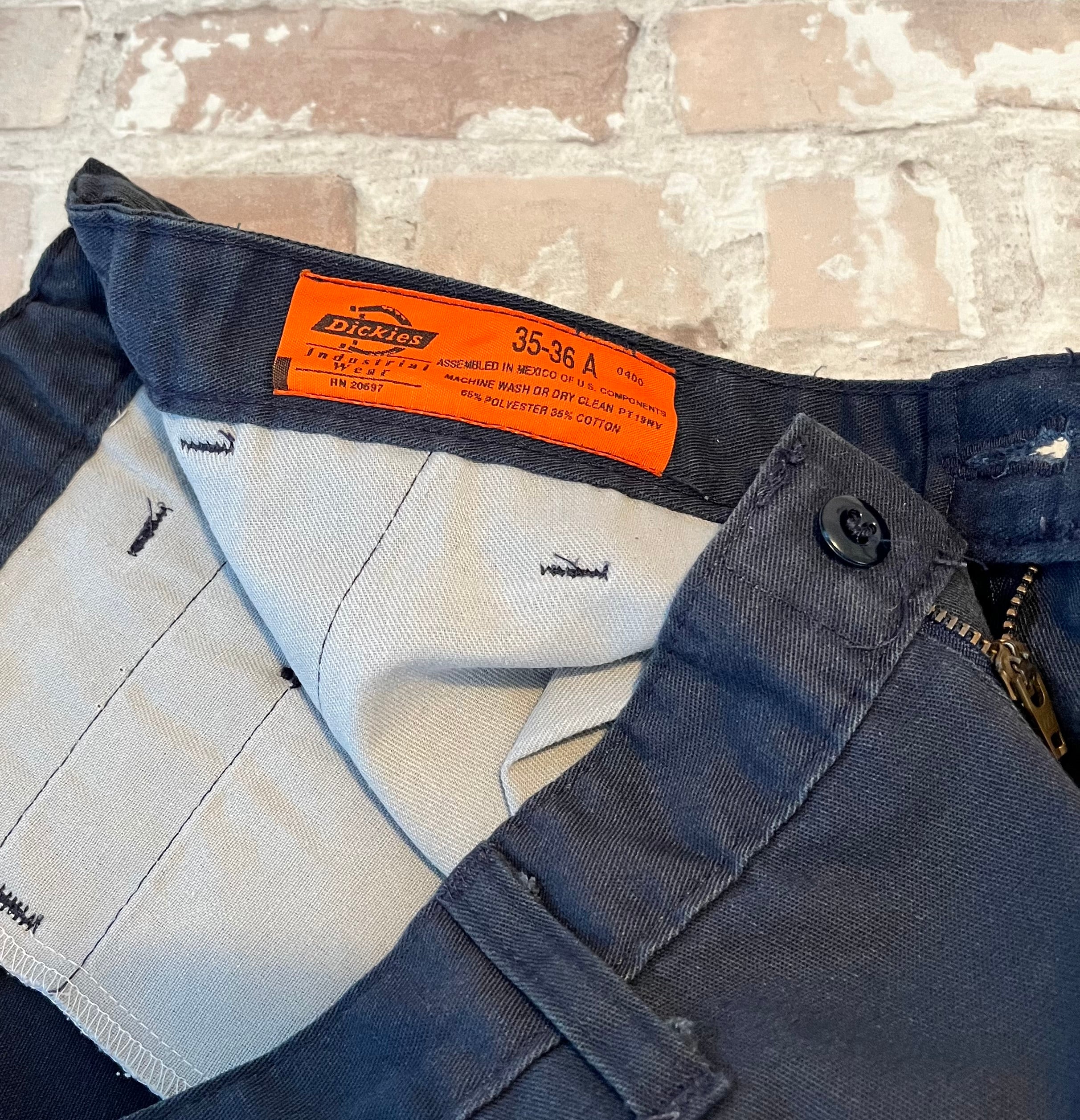 Gros plan sur l'étiquette vintage orange Dickies Industrial et les inserts élastiques de la ceinture d'un short de travail.