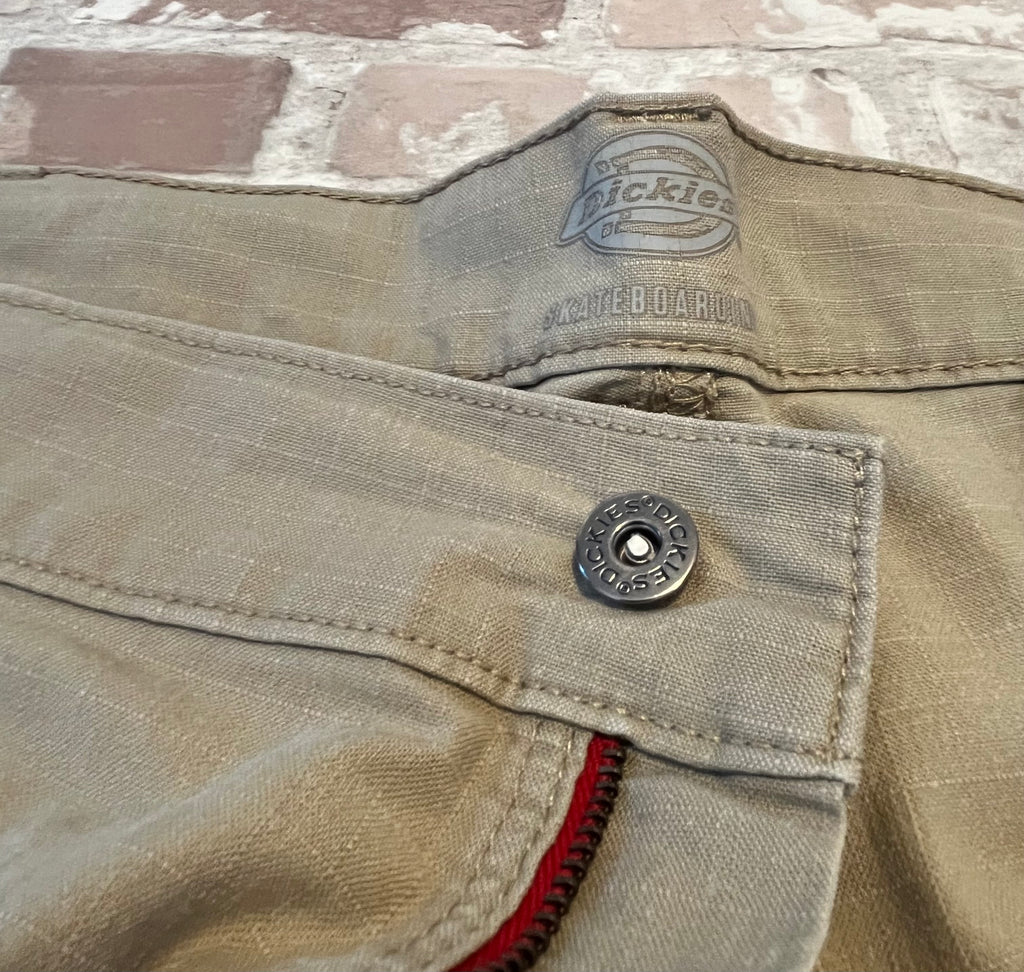 Gros plan sur la fermeture éclair rouge contrastée et le bouton métallique griffé d'un short cargo Dickies.