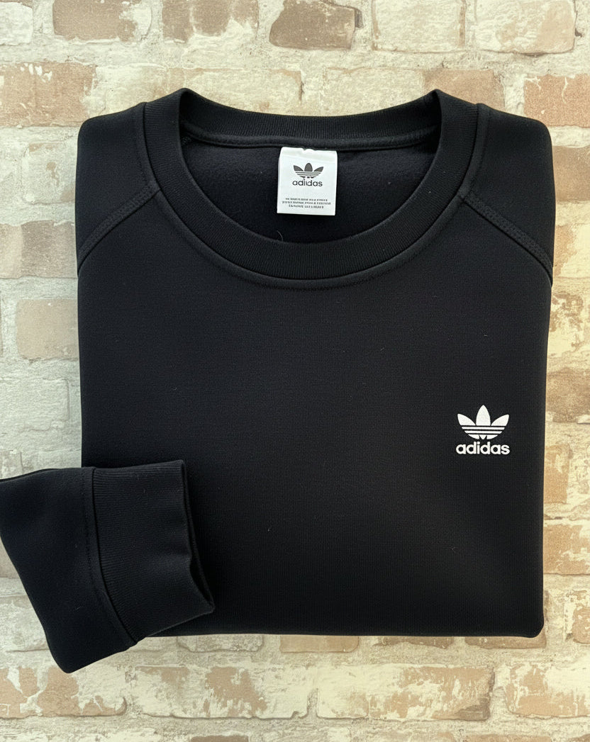 Sweat col rond vintage Adidas Originals noir avec l'iconique logo trèfle blanc brodé sur la poitrine, présenté plié à plat.