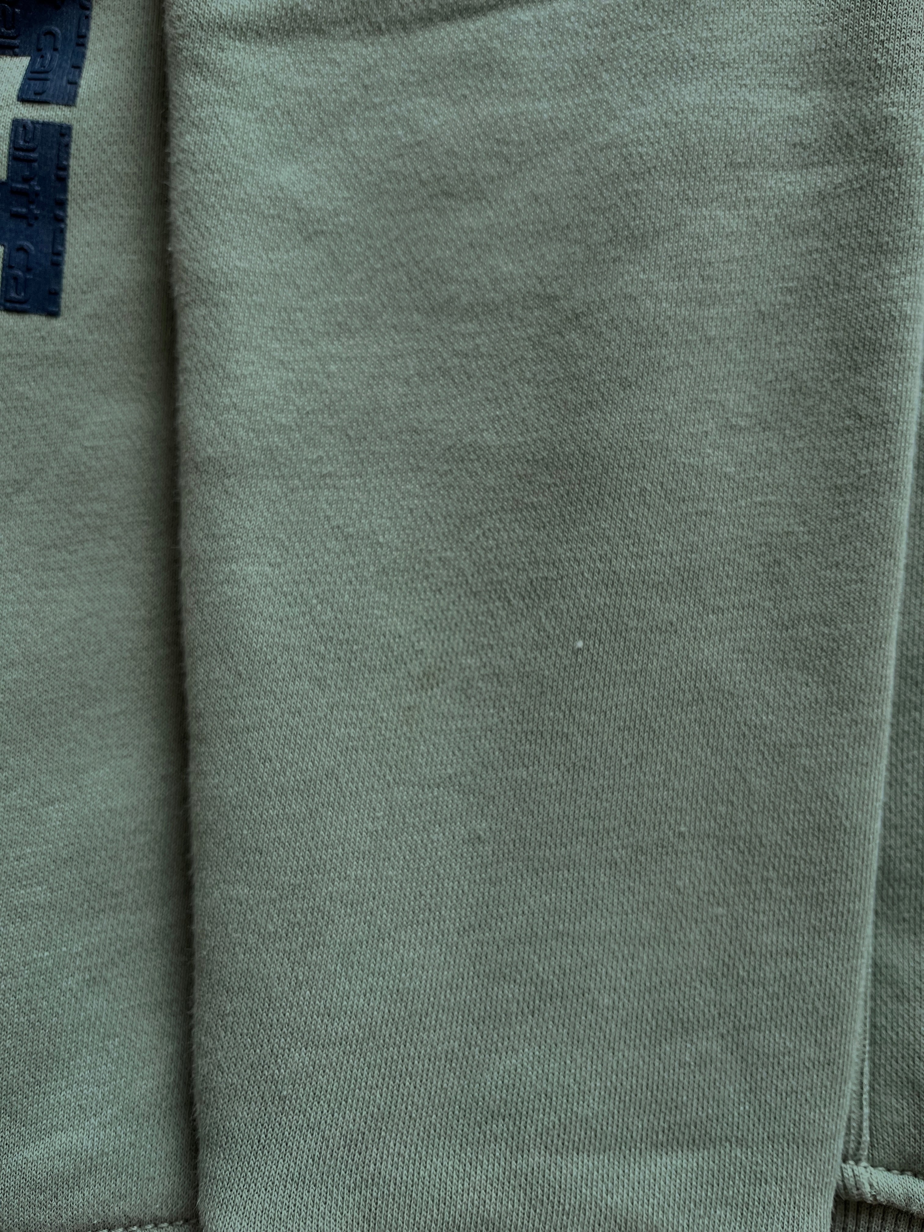 Détail d'une discrète trace d'usage sur la manche d'un sweat de seconde main Carhartt vert sauge.